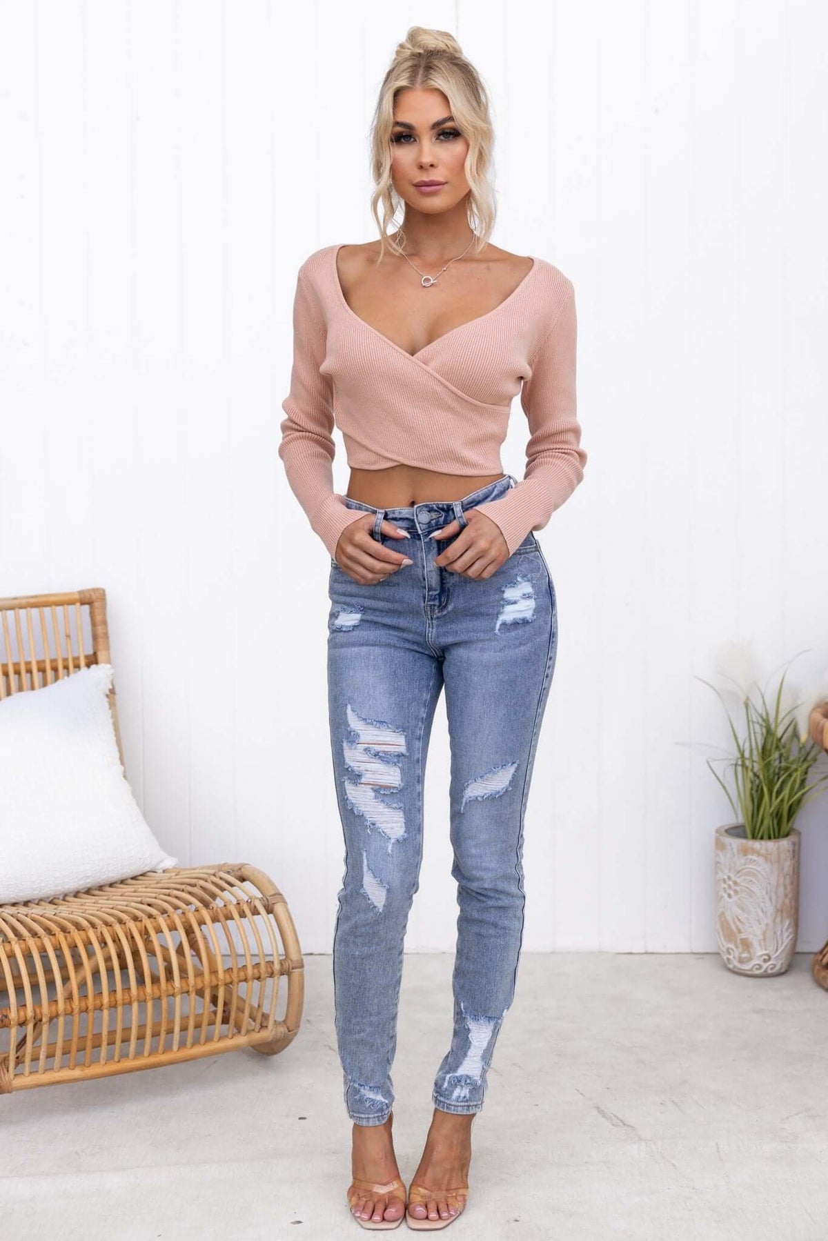 Woman wearing a pink Selby Top with a V-neckline, styled with distressed jeans and heels, showcasing a trendy casual look.