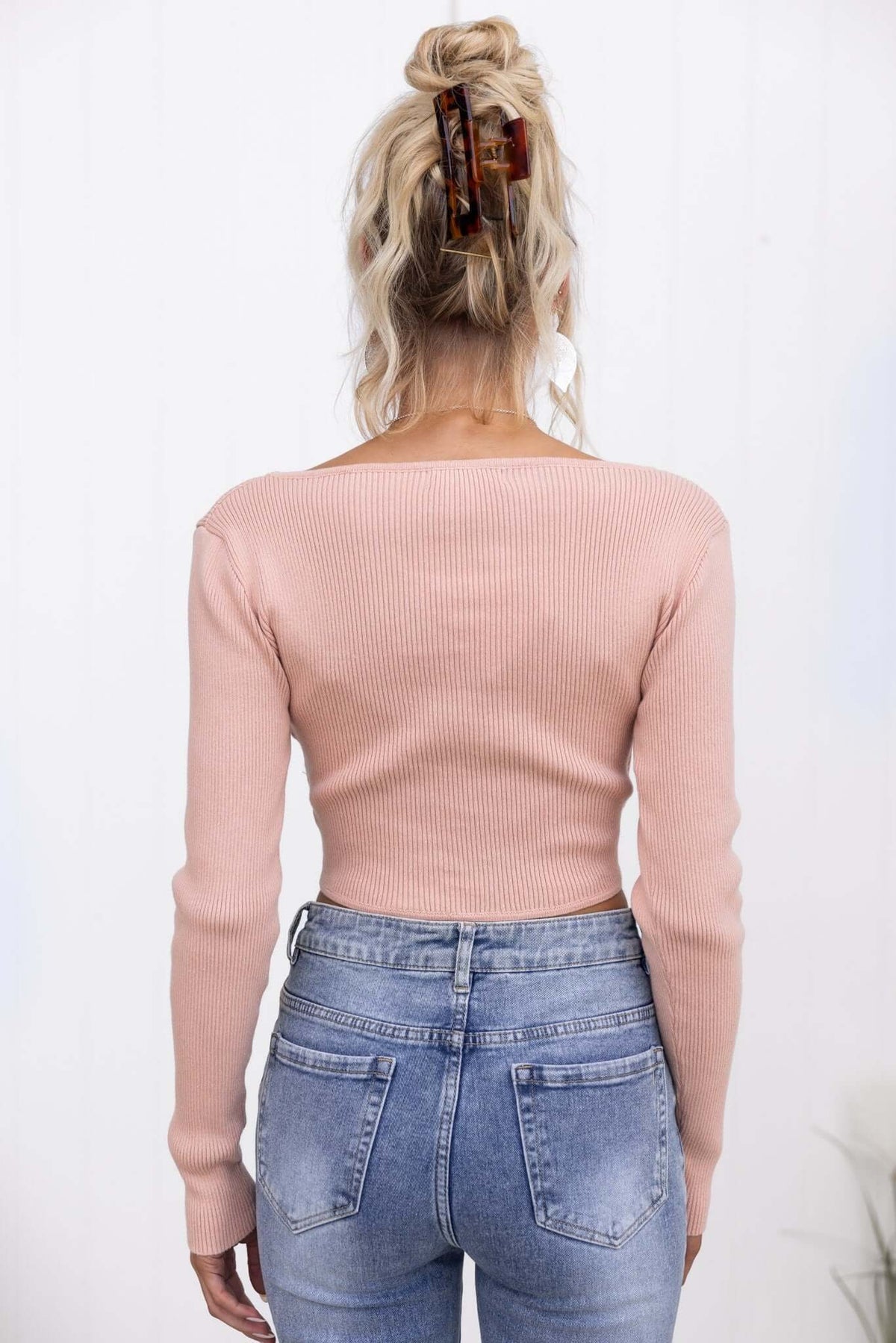 Back view of a model wearing a pink ribbed Selby Top with V-neckline, paired with high-waisted denim jeans.