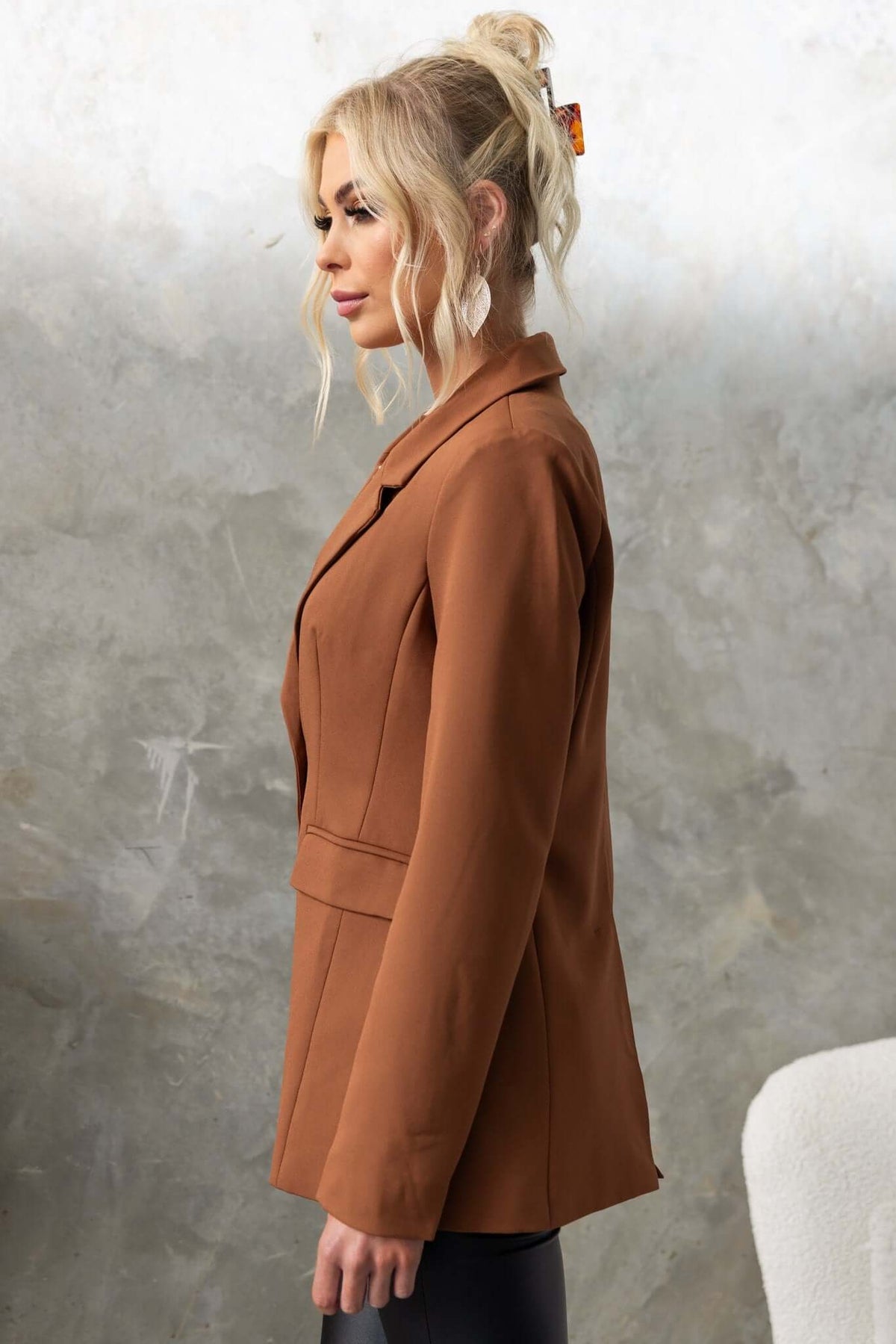 Side view of a woman in a brown Desio Blazer with shoulder pads and front pockets, styled with sleek hair.