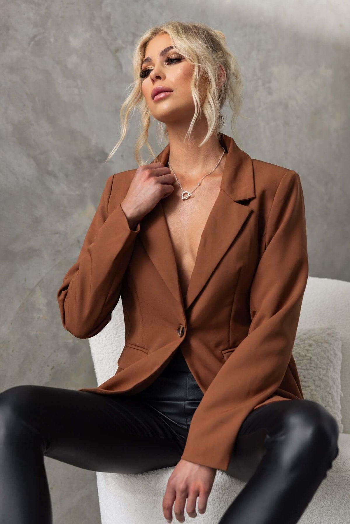 Stylish woman wearing a brown Desio blazer with a V-neck, seated in a modern setting, showcasing a chic and elegant look.
