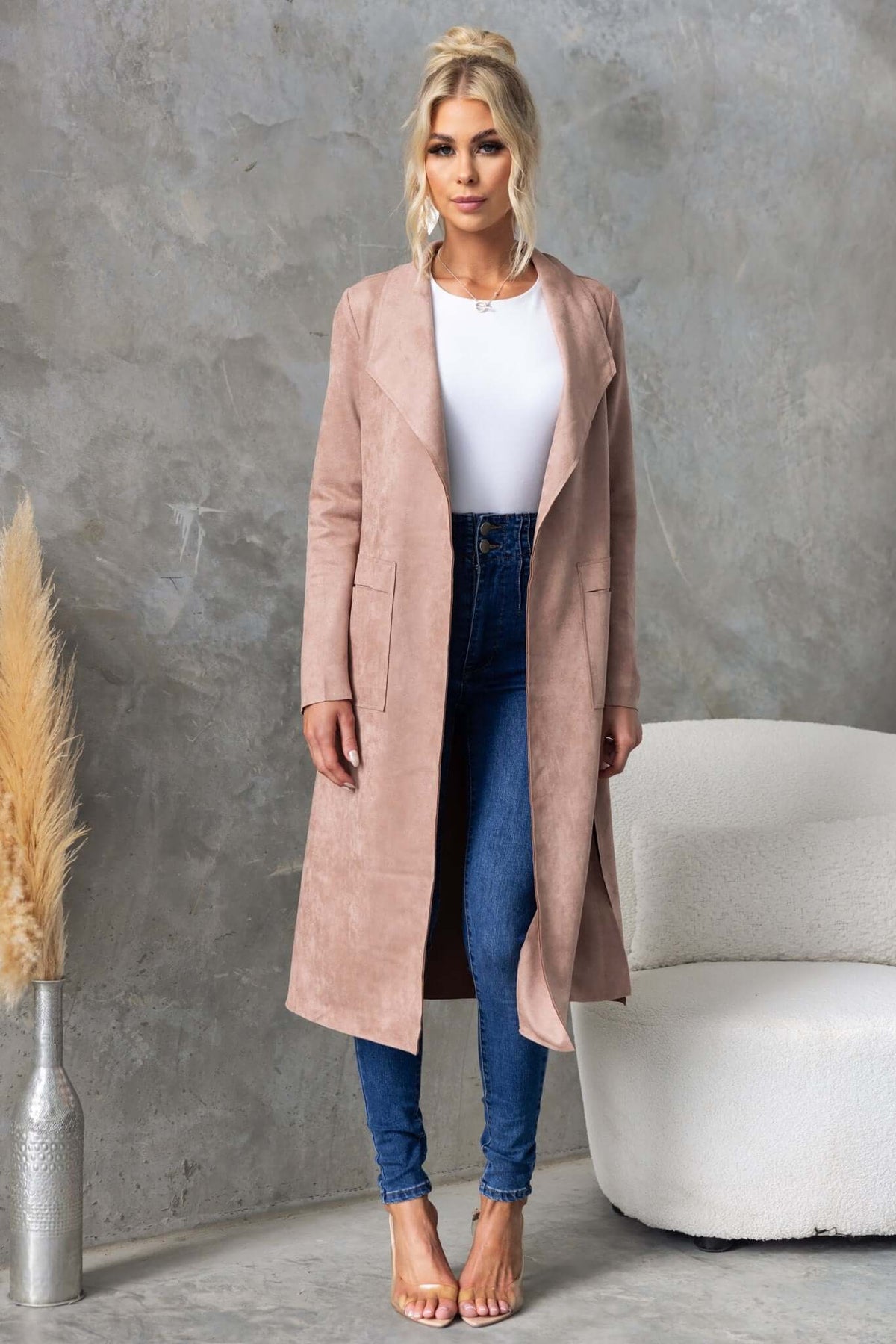Model wearing Hayley Coat with draping lapel, side slits, and pockets paired with blue jeans against a textured backdrop.