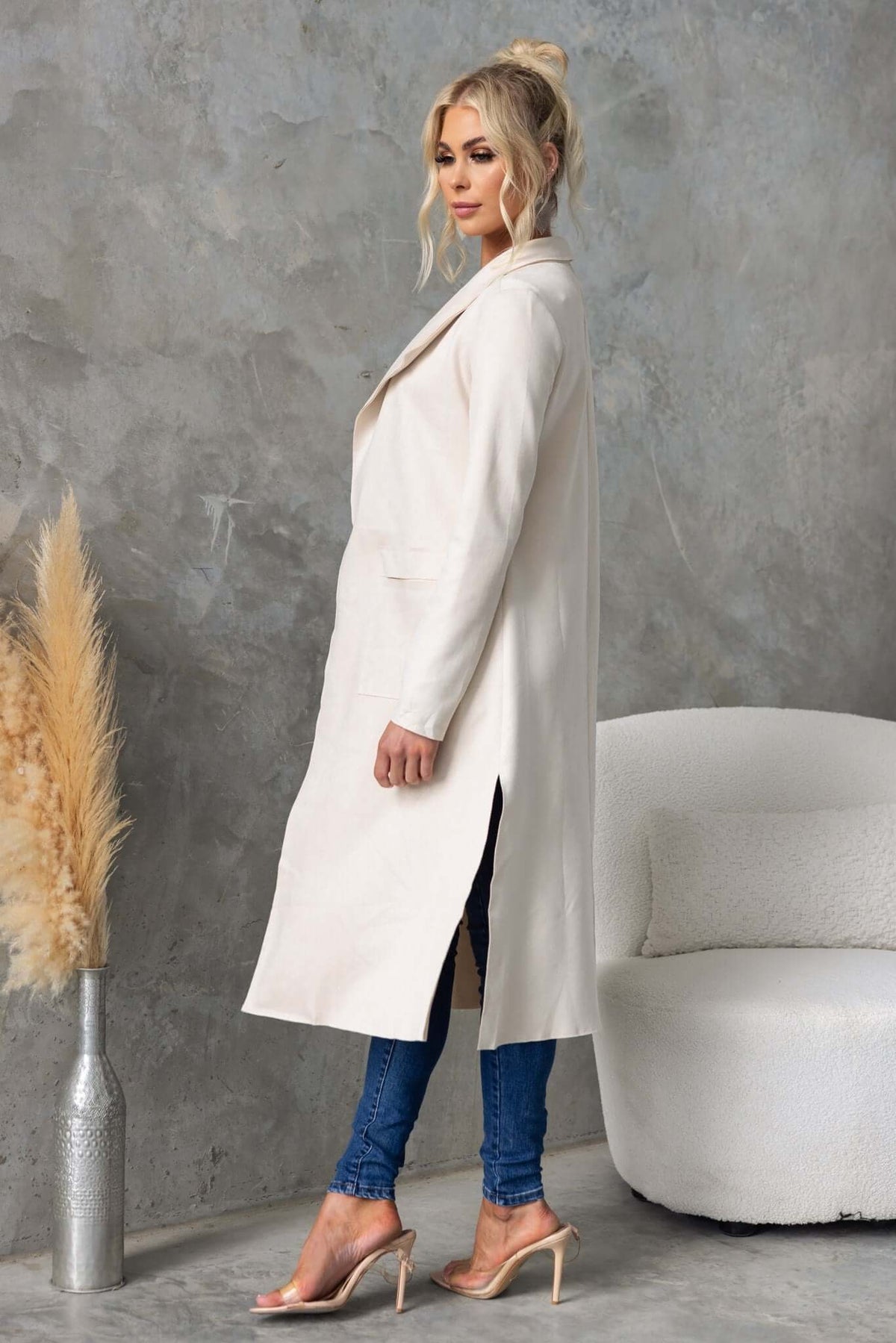 Model wearing a longline Hayley coat with draping lapel, high slits, and pockets over denim jeans.