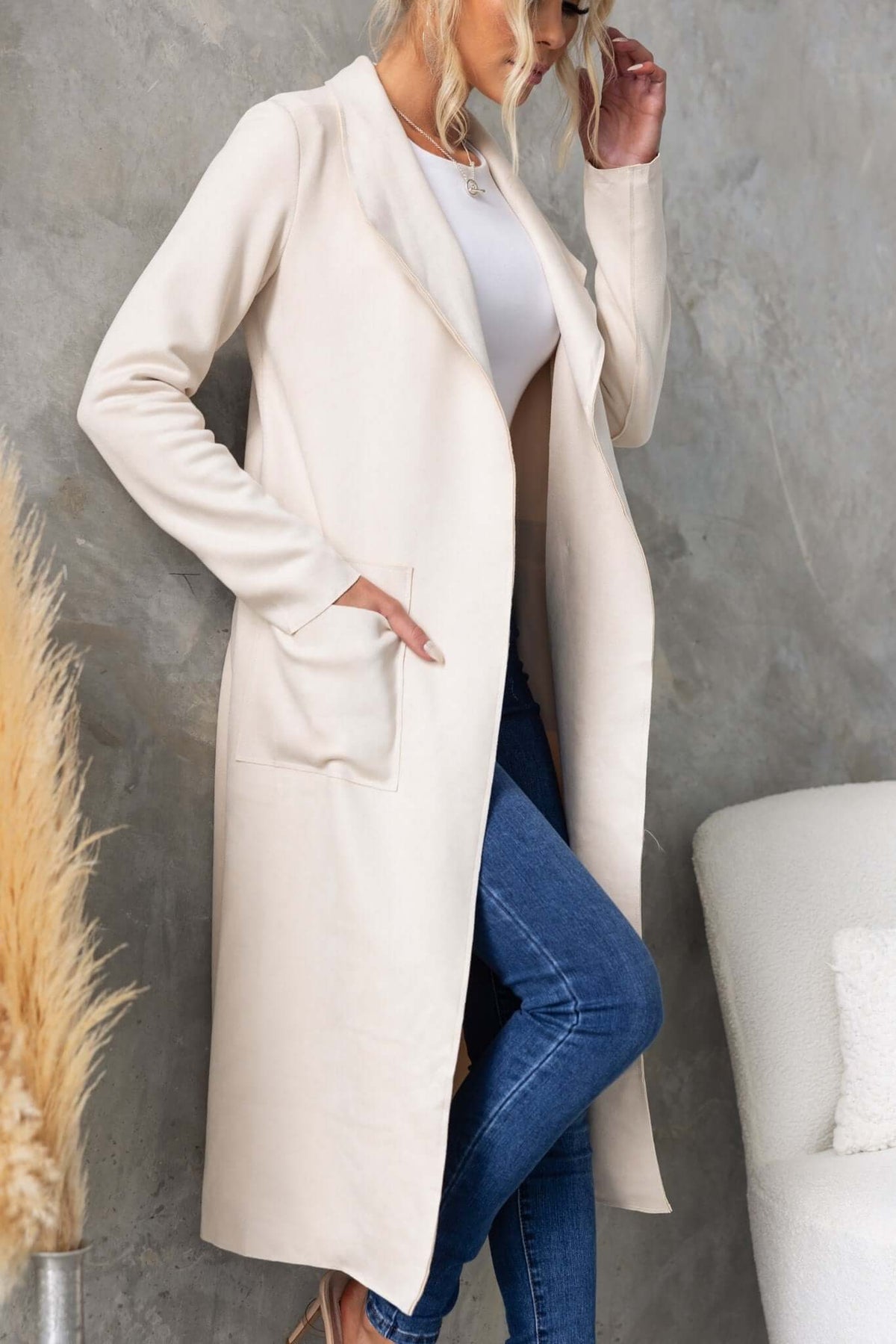 Model wearing the Hayley Coat in cream, featuring a longline fit, draped lapel, pockets, and high slits.