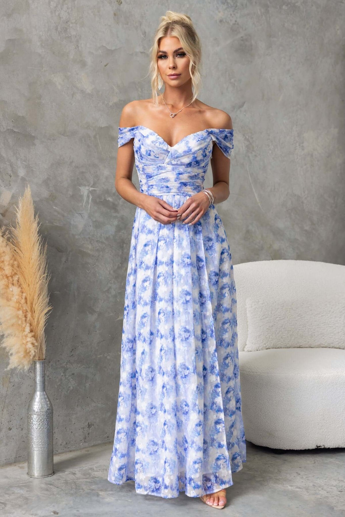 Joan Maxi Dress in blue floral design, featuring off-the-shoulder sleeves and flowing skirt, styled against textured background.