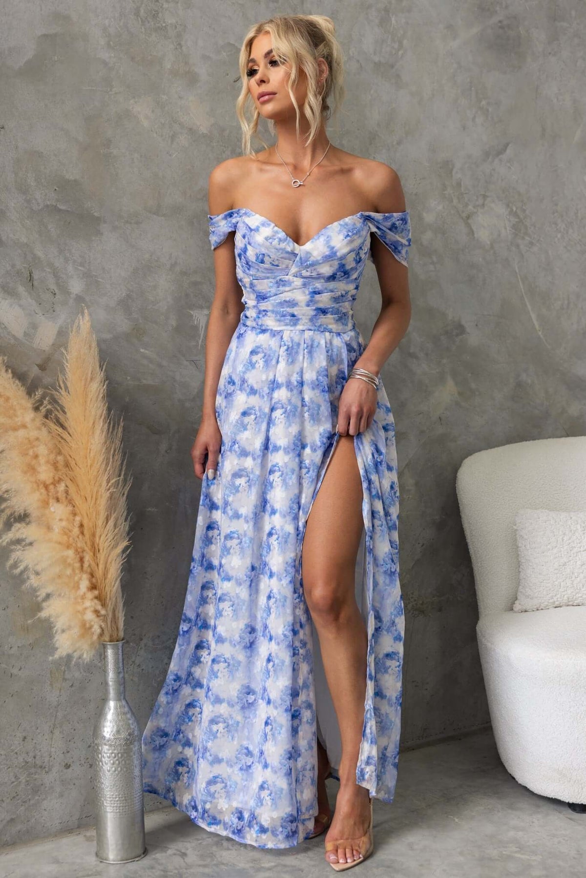 Joan Maxi Dress in blue floral print with off-shoulder design and thigh-high slit, styled with minimalist accessories.