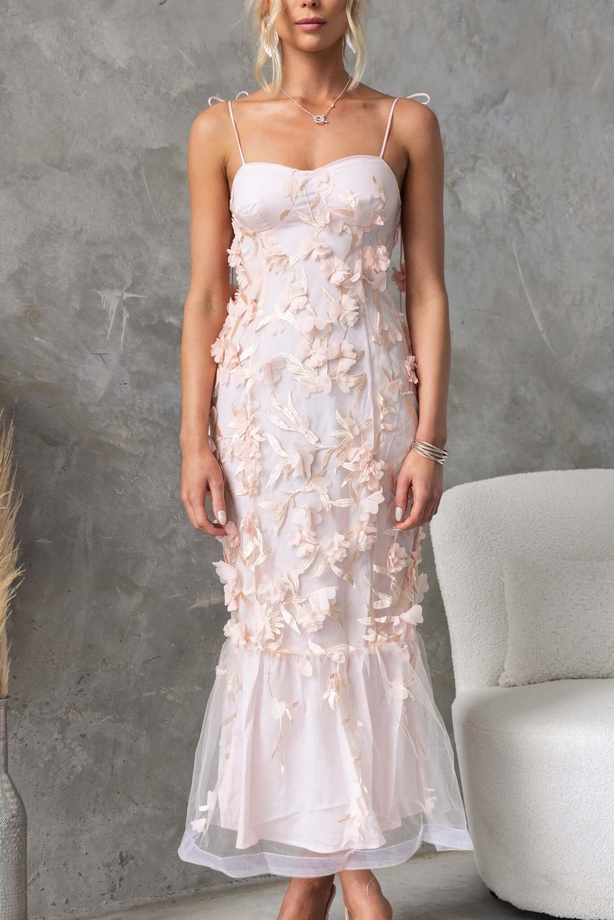 Nephi Midi Dress featuring adjustable tie straps and lace overlay, modeled in soft pink on a textured backdrop.