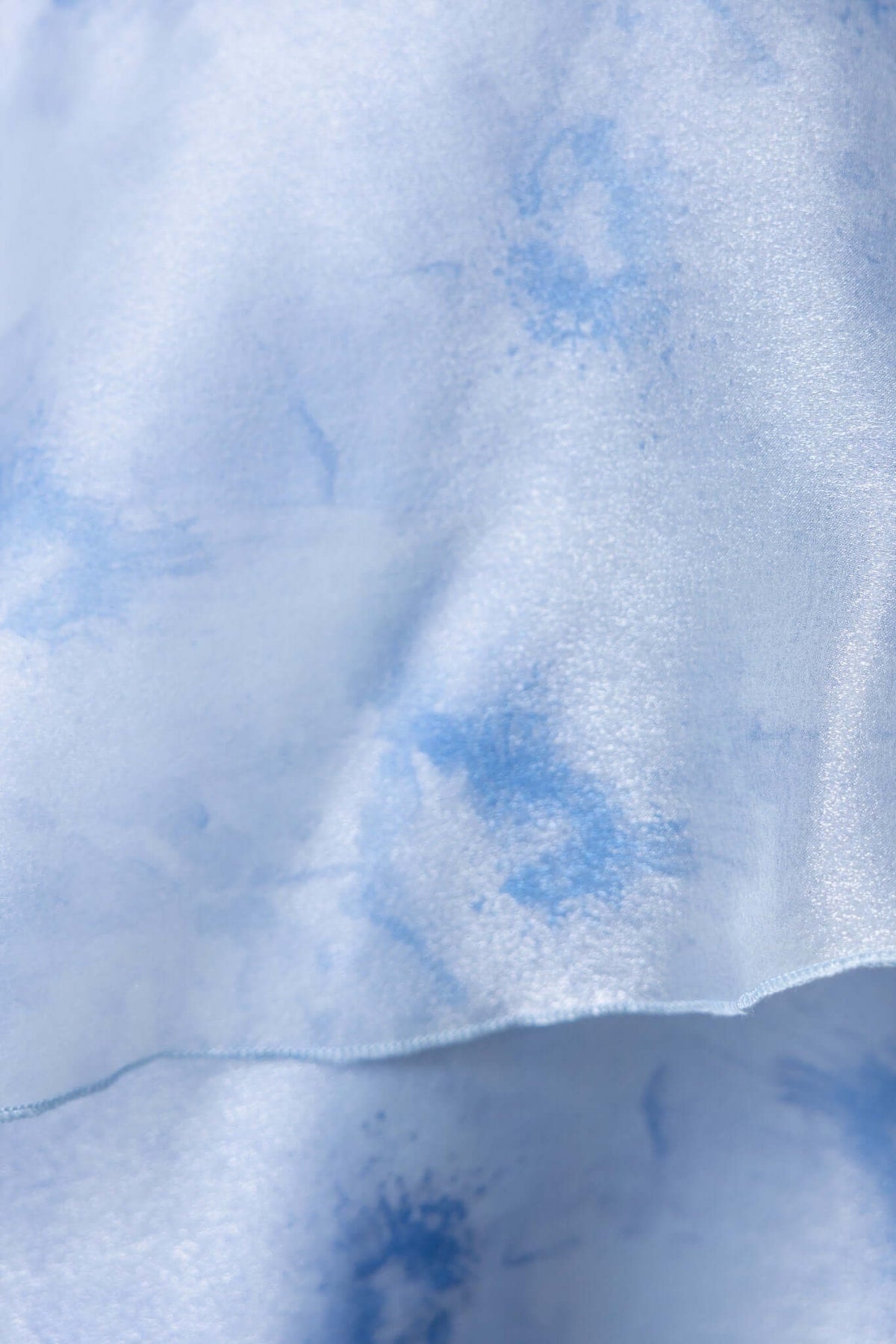 Close-up of light blue chiffon fabric with a subtle watercolor pattern, showcasing the texture and color details.