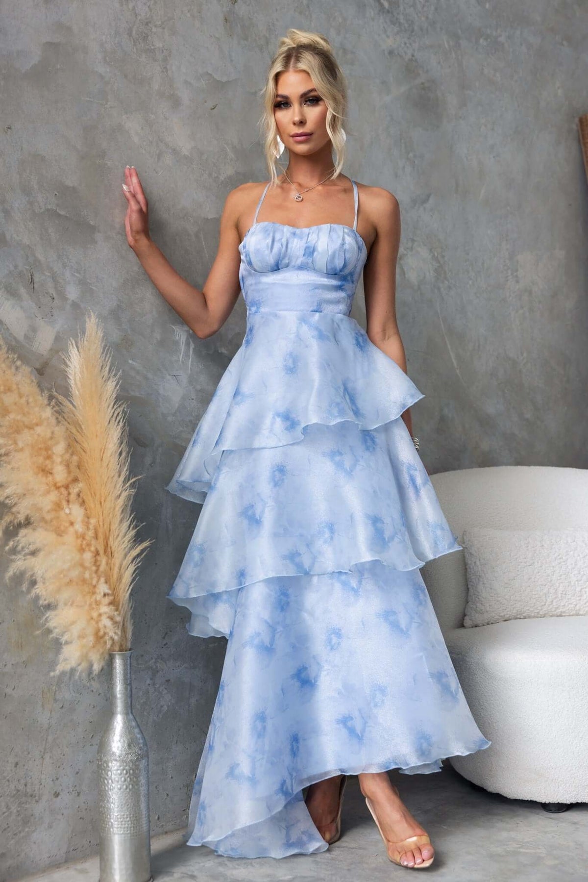 Kirsti Maxi Dress in light blue chiffon with ruffle layers and adjustable tie straps, modeled in a chic indoor setting.