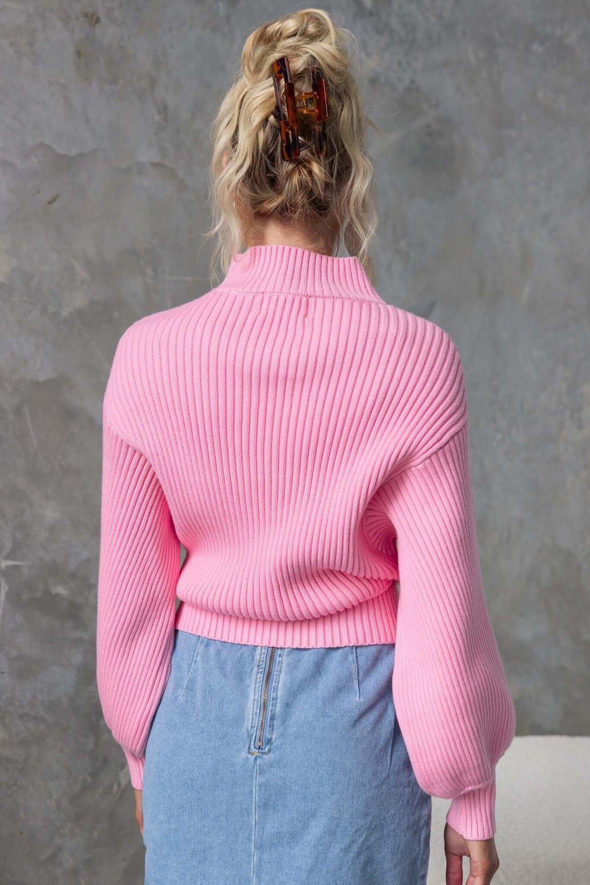 Back view of a model in a pink ribbed Sola Jumper with wide sleeves, paired with a denim skirt.