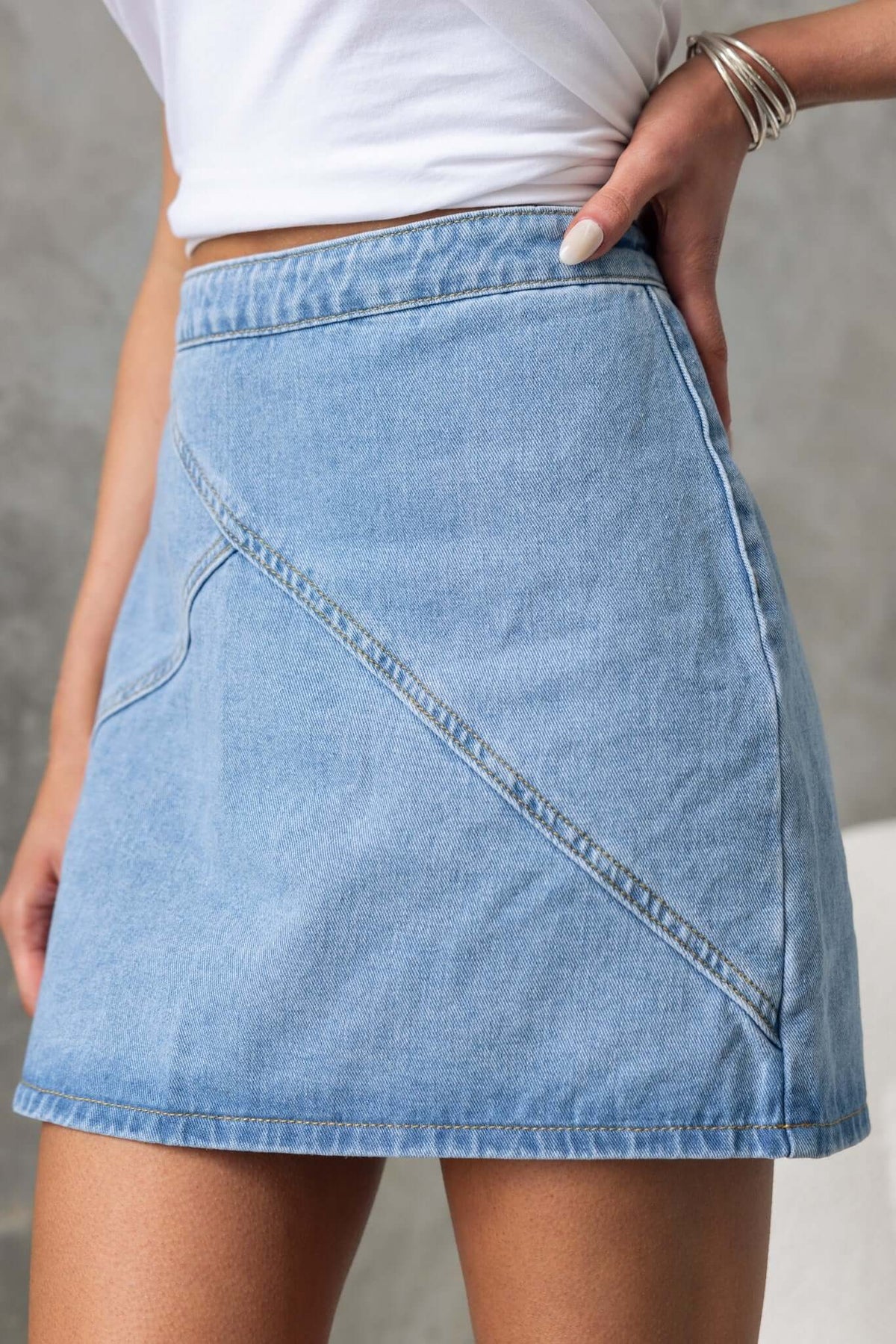 Lizzie Denim Skirt with mid-high waist fit in light blue, featuring angled seam detail and sleek silhouette.