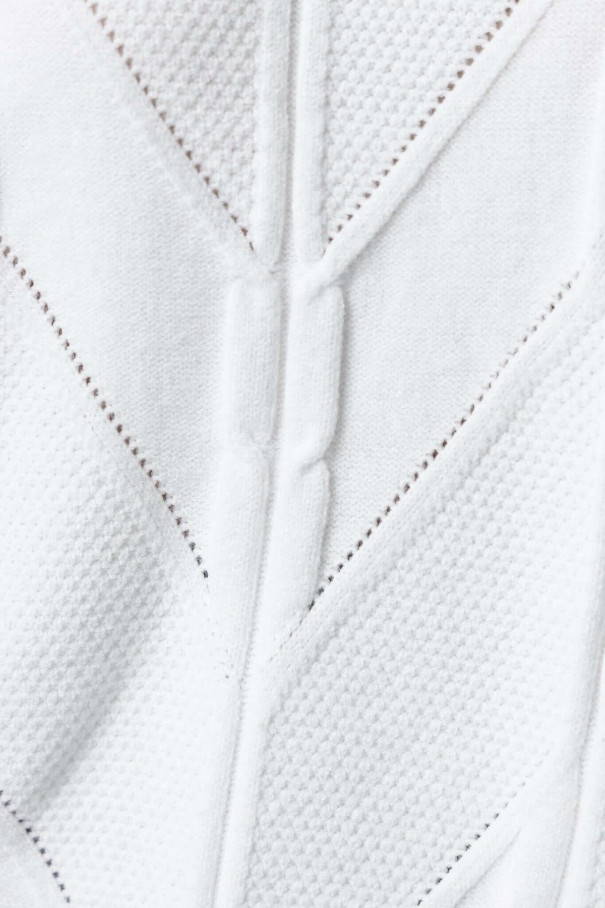 Close-up of Becker Jumper texture, showcasing intricate cable knit details in a soft white fabric.