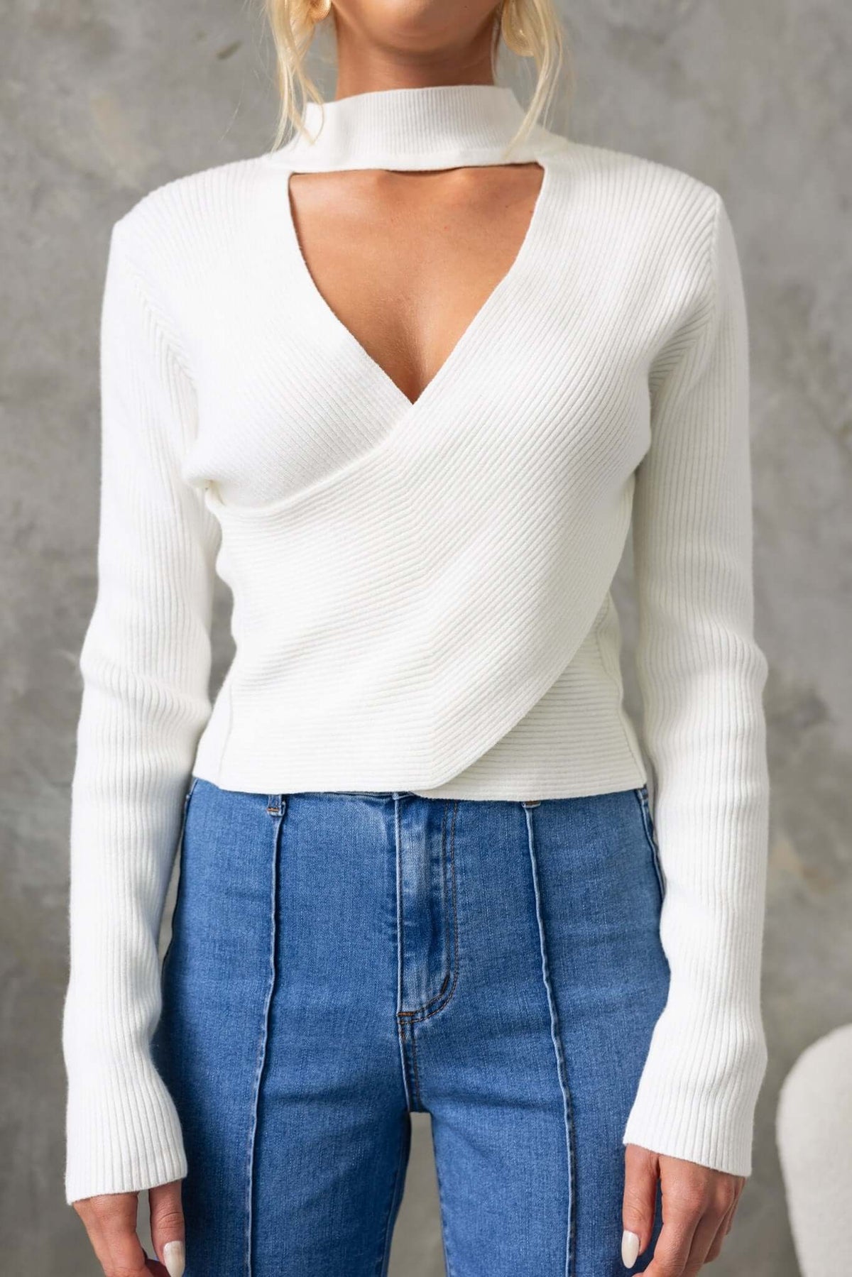 Inala Top: ribbed knit white top with high neckline and cross-over detailing, styled with blue high-waisted jeans.