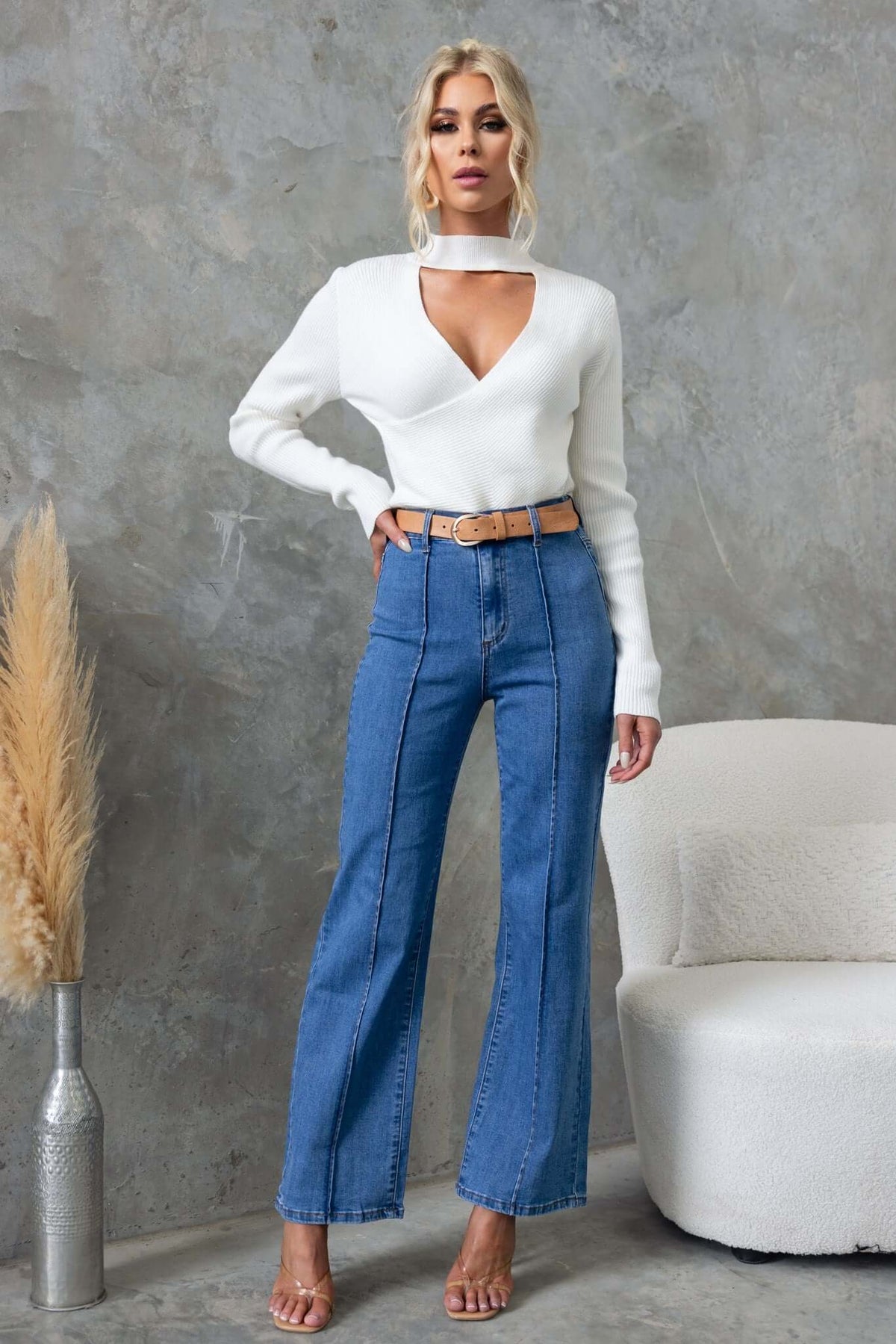 Model wearing a white ribbed knit Inala Top with cross-over detail, paired with high-waisted blue jeans styled with a belt.