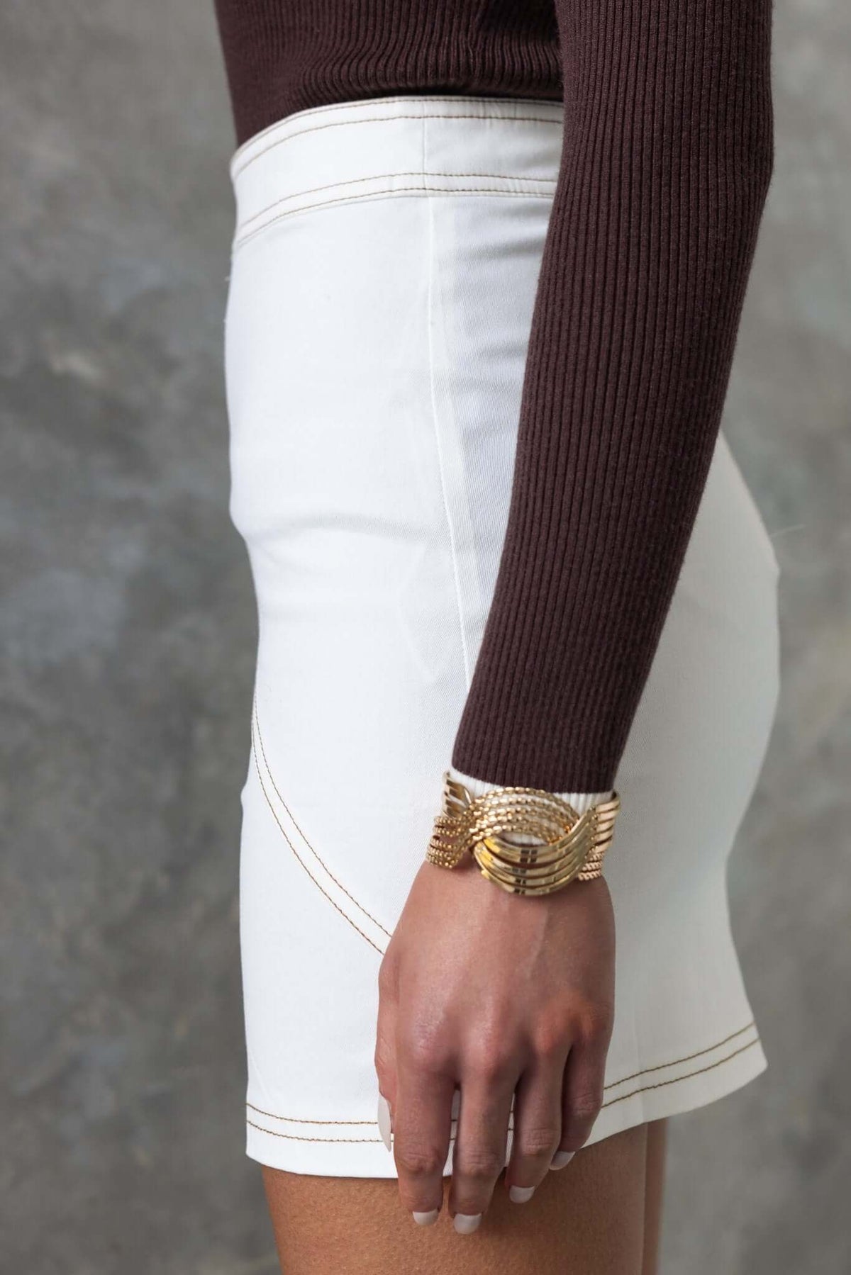 Model showcasing Elko Skirt in white, featuring mid-high waist and back zip, paired with a brown sweater.