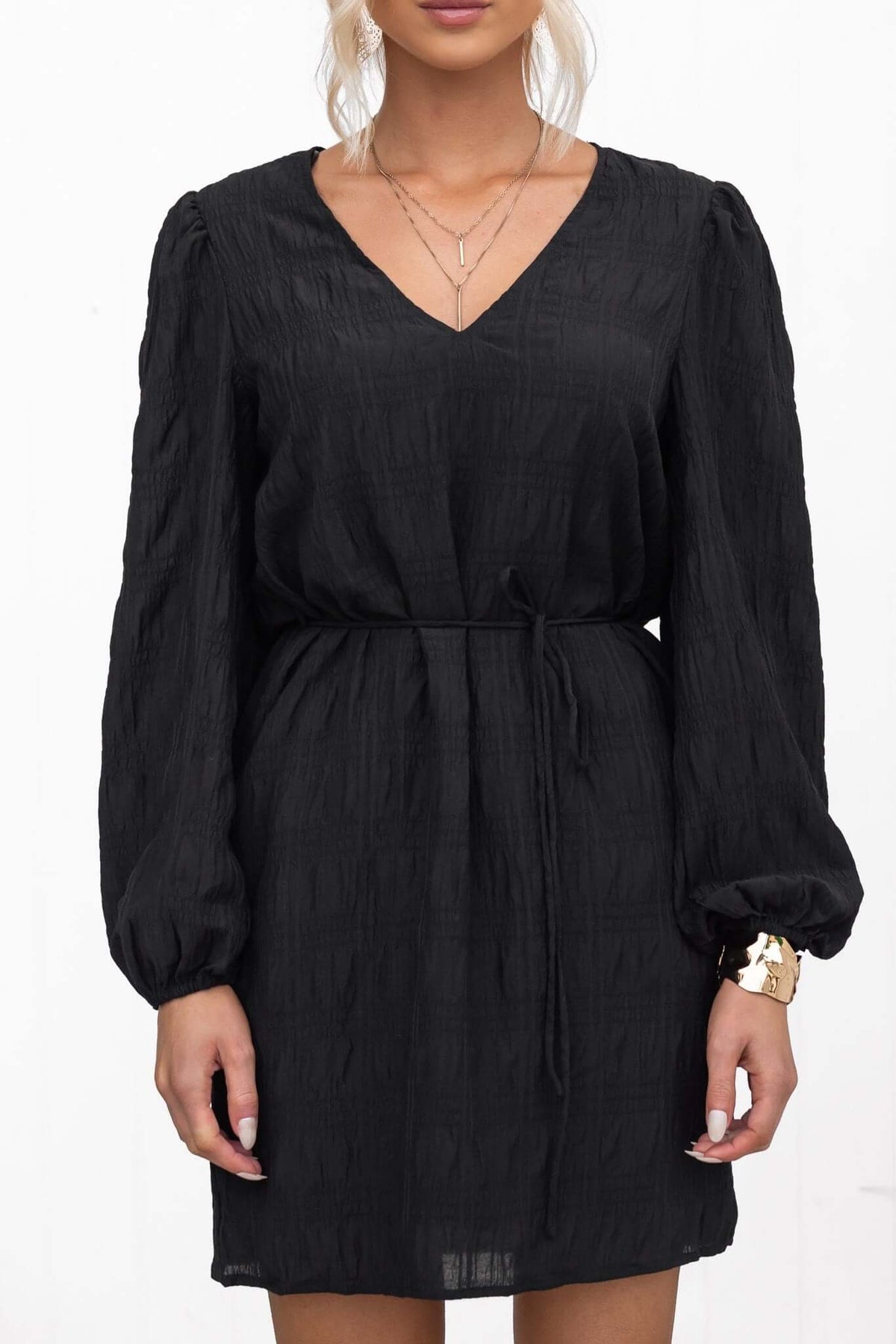 Black V-neck dress with removable tie, elastic sleeves, and pockets, featuring textured material and a relaxed fit.