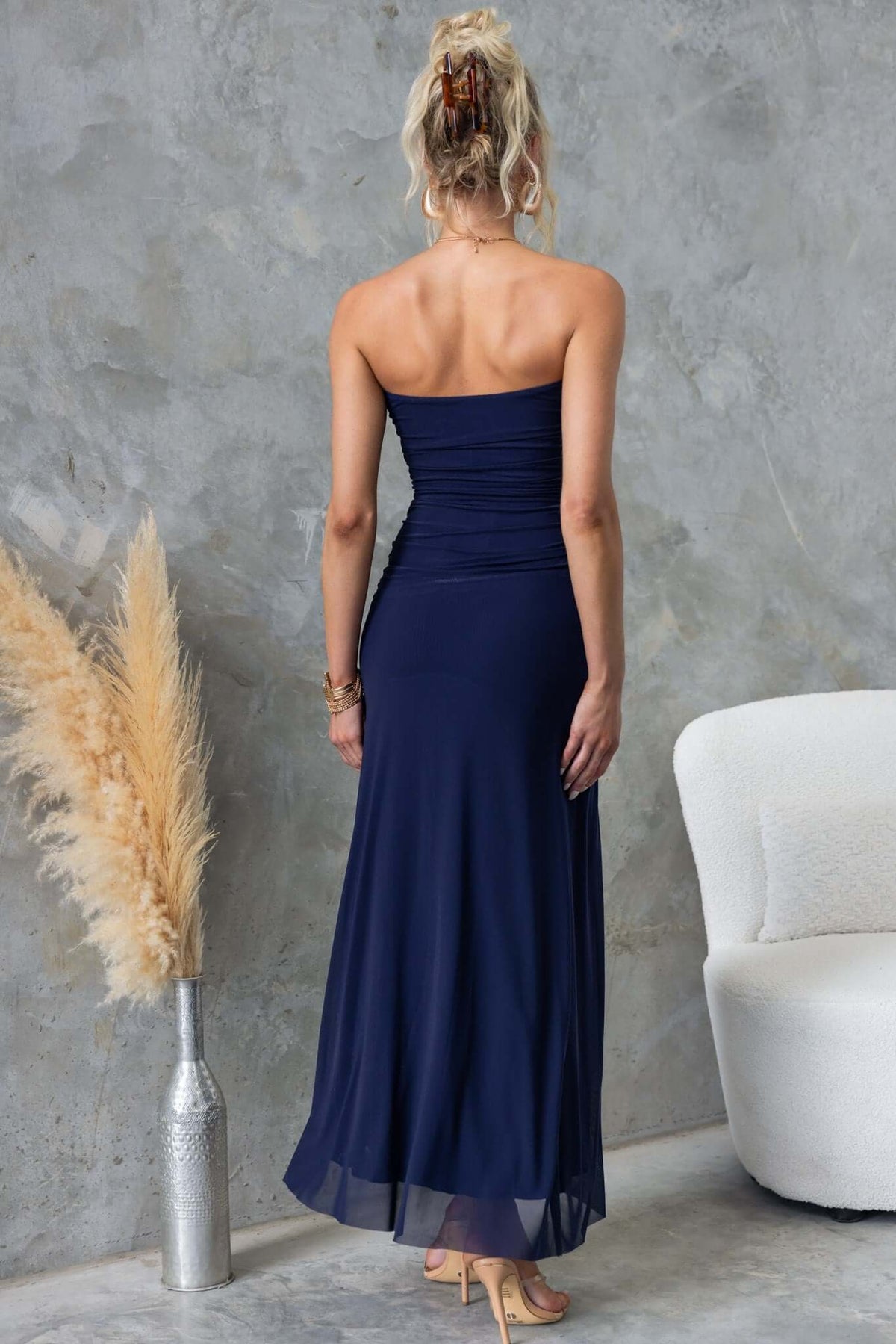 Back view of a woman wearing a navy strapless maxi dress with a fitted bodice and flowing skirt.