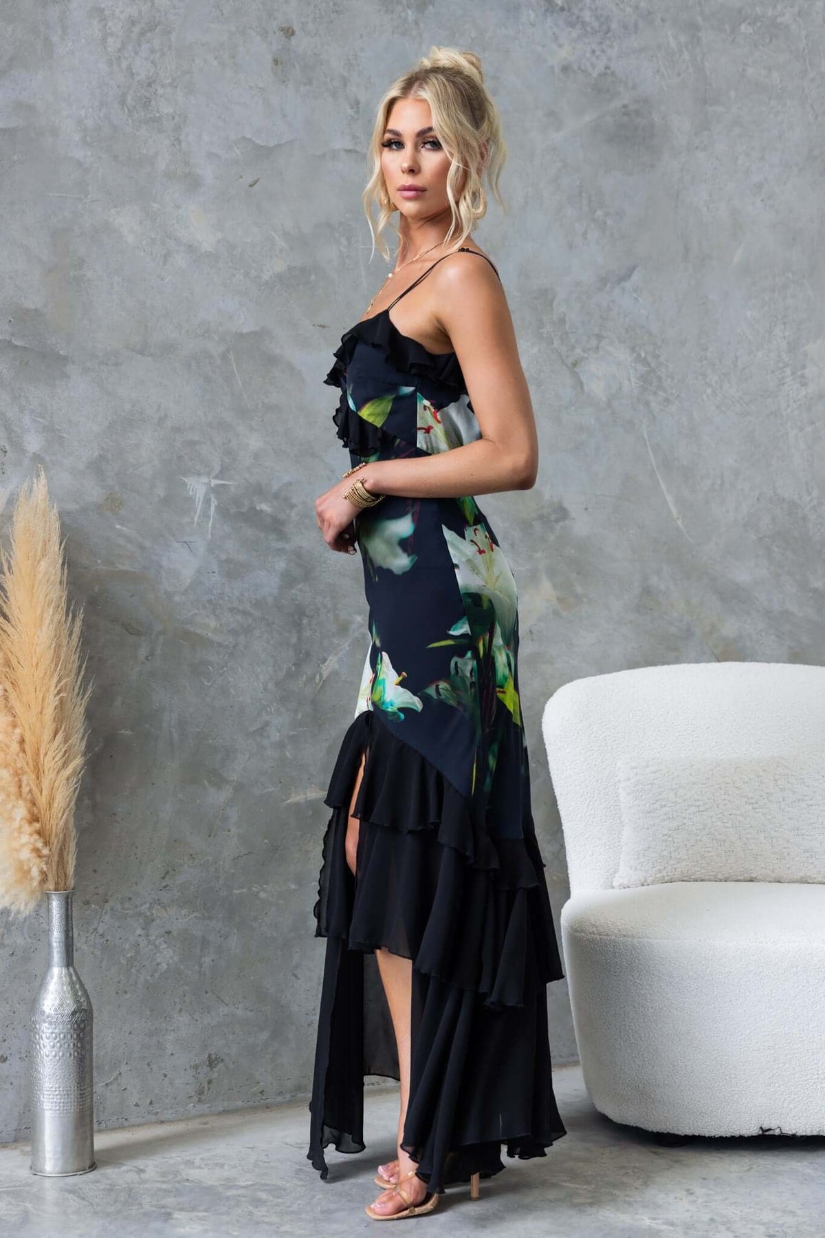 Black floral maxi dress with ruffles, adjustable straps, and front split, styled with a chic background.