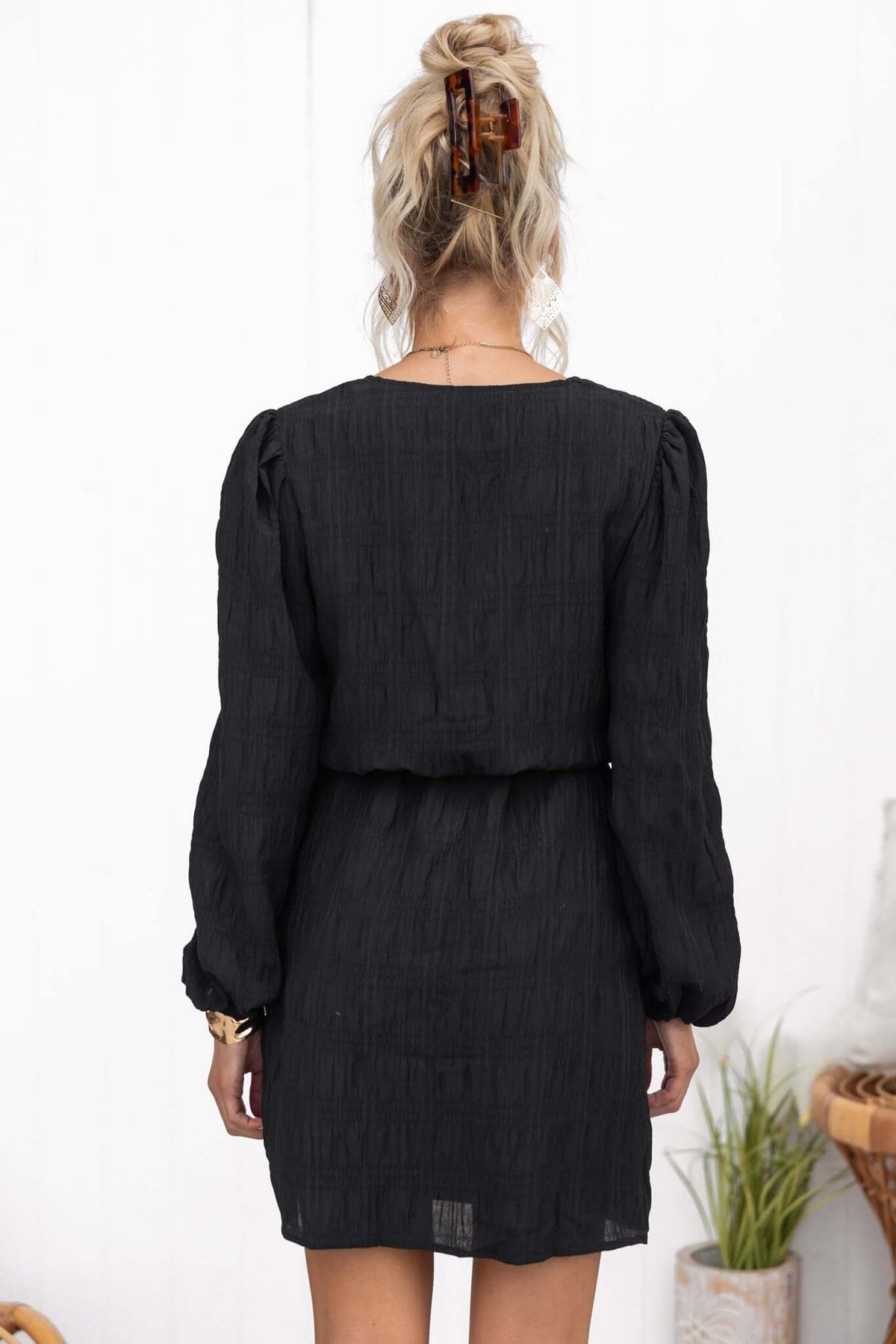 Back view of the Davis Dress featuring a textured black fabric, V-neckline, and elastic sleeves.