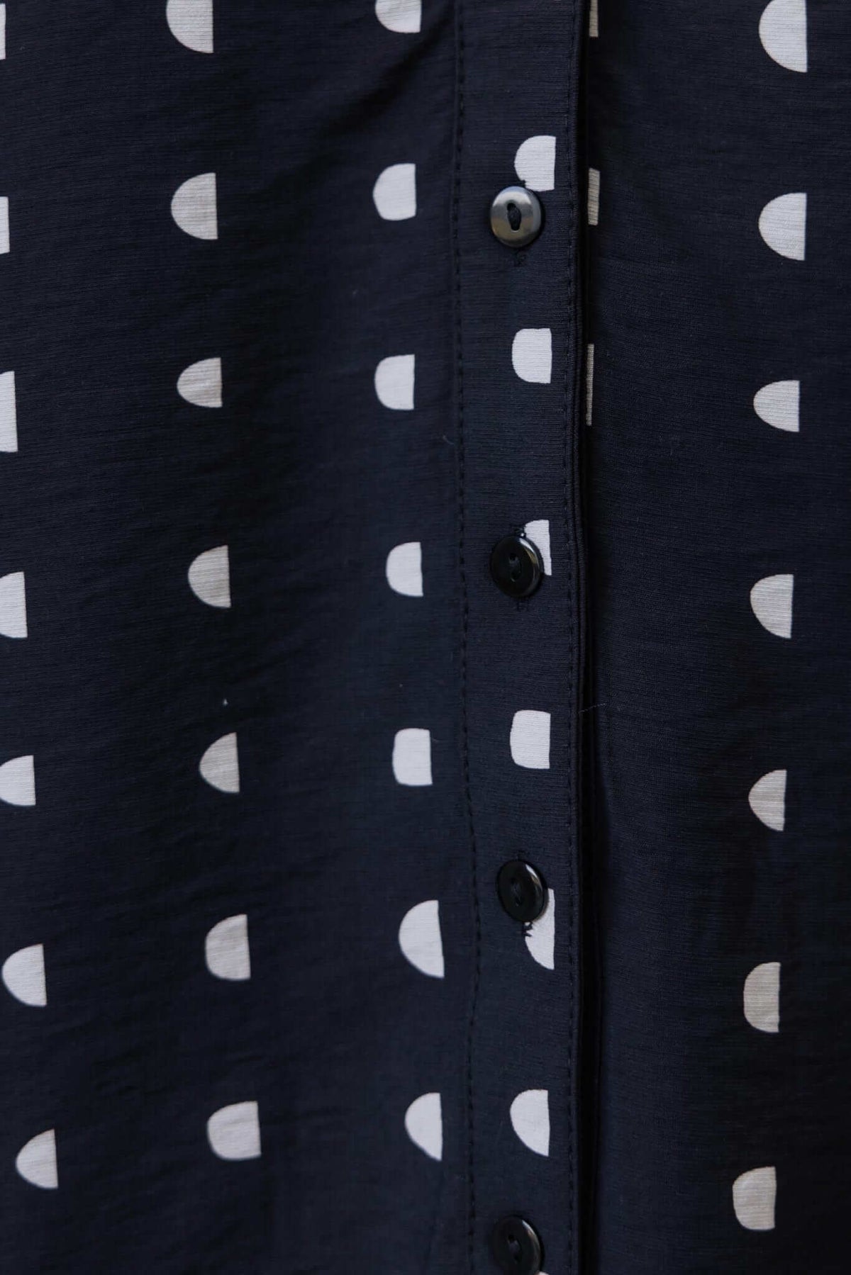 Close-up of black shirt with white polka dots and button-up details, showcasing textured fabric.