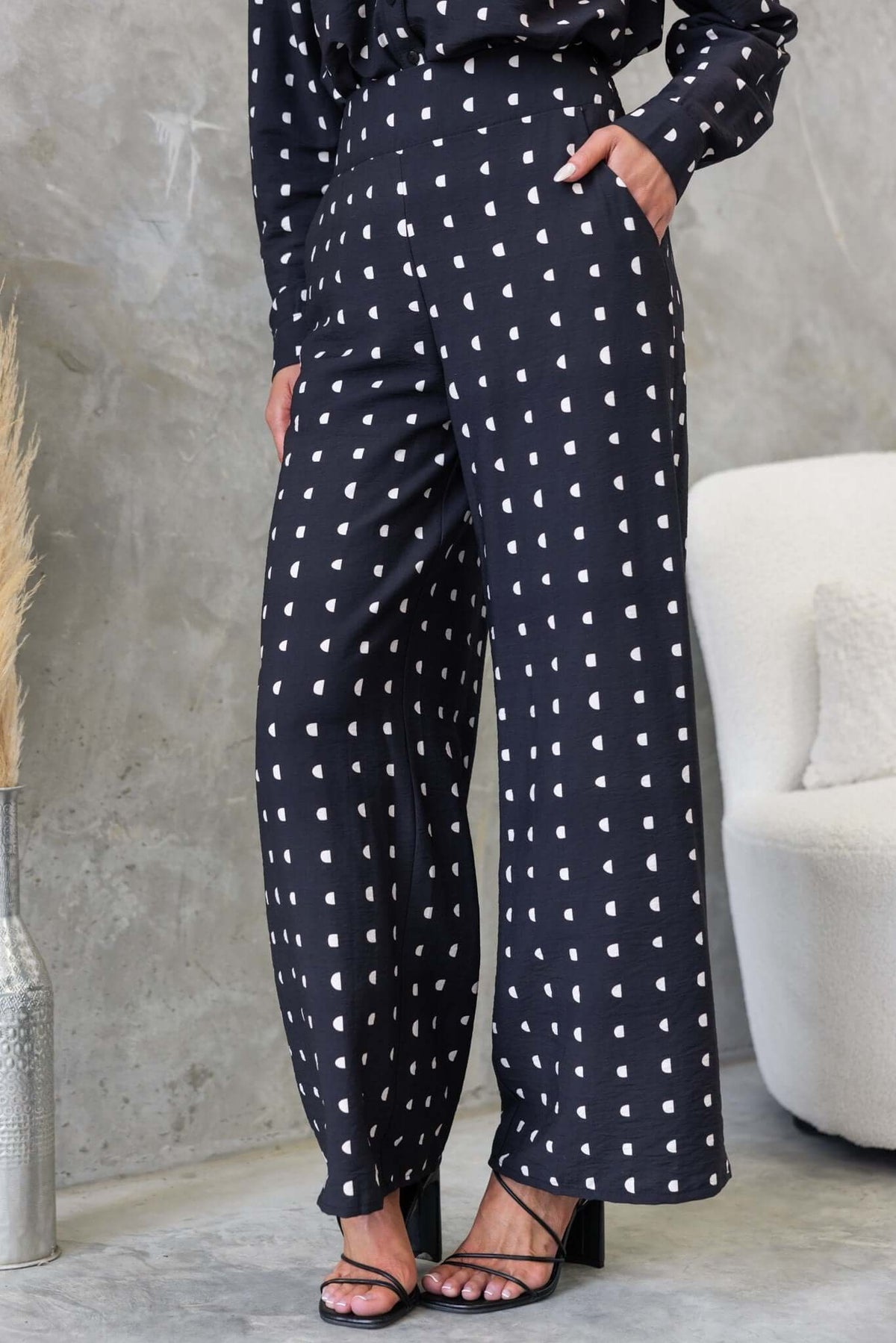 Marion Pants in black with white hearts, featuring a mid-high waist, elastic back, and side pockets, styled with heeled sandals.