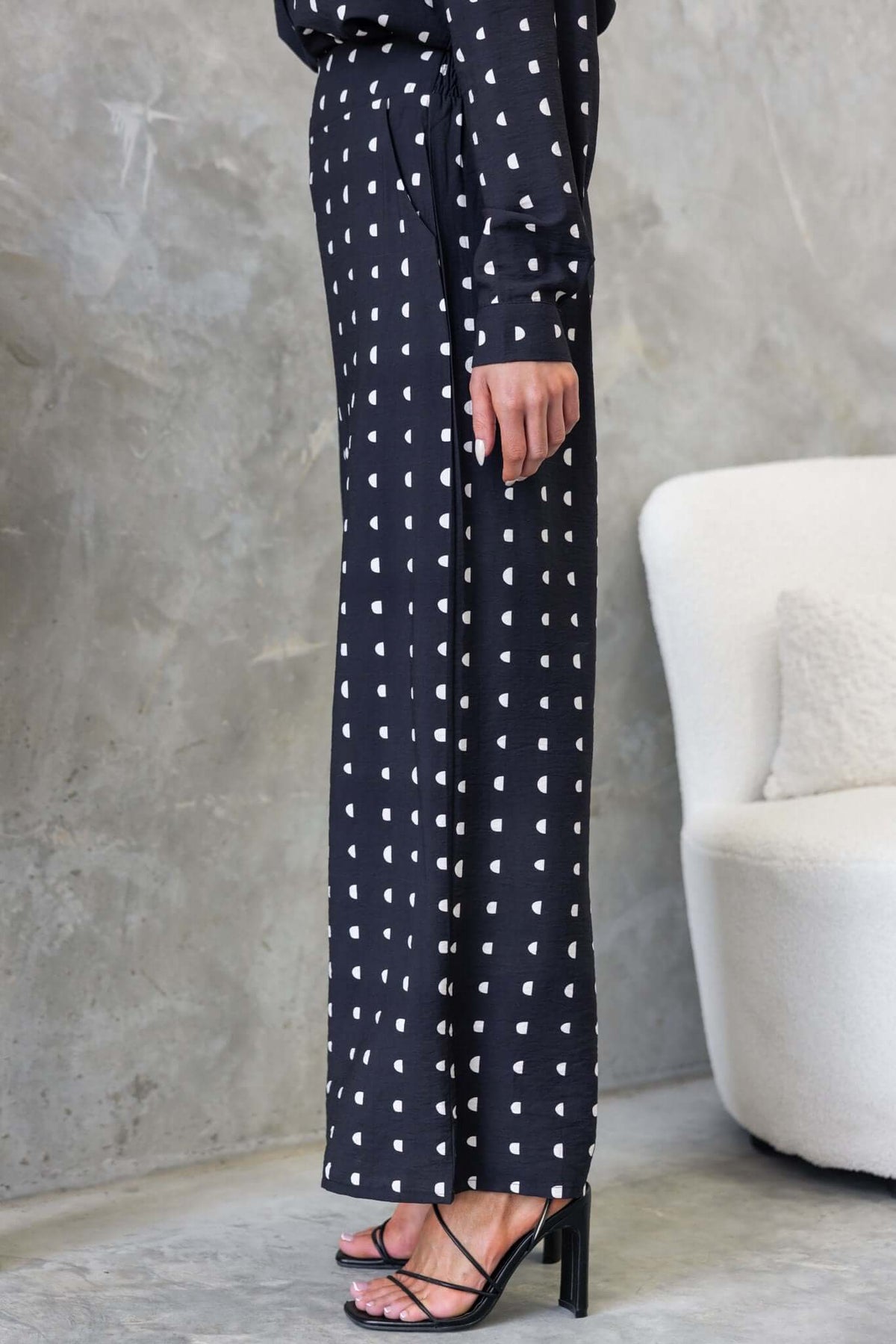 Side view of Marion Pants featuring a mid-high waist, textured black fabric with white hearts, paired with stylish heels.