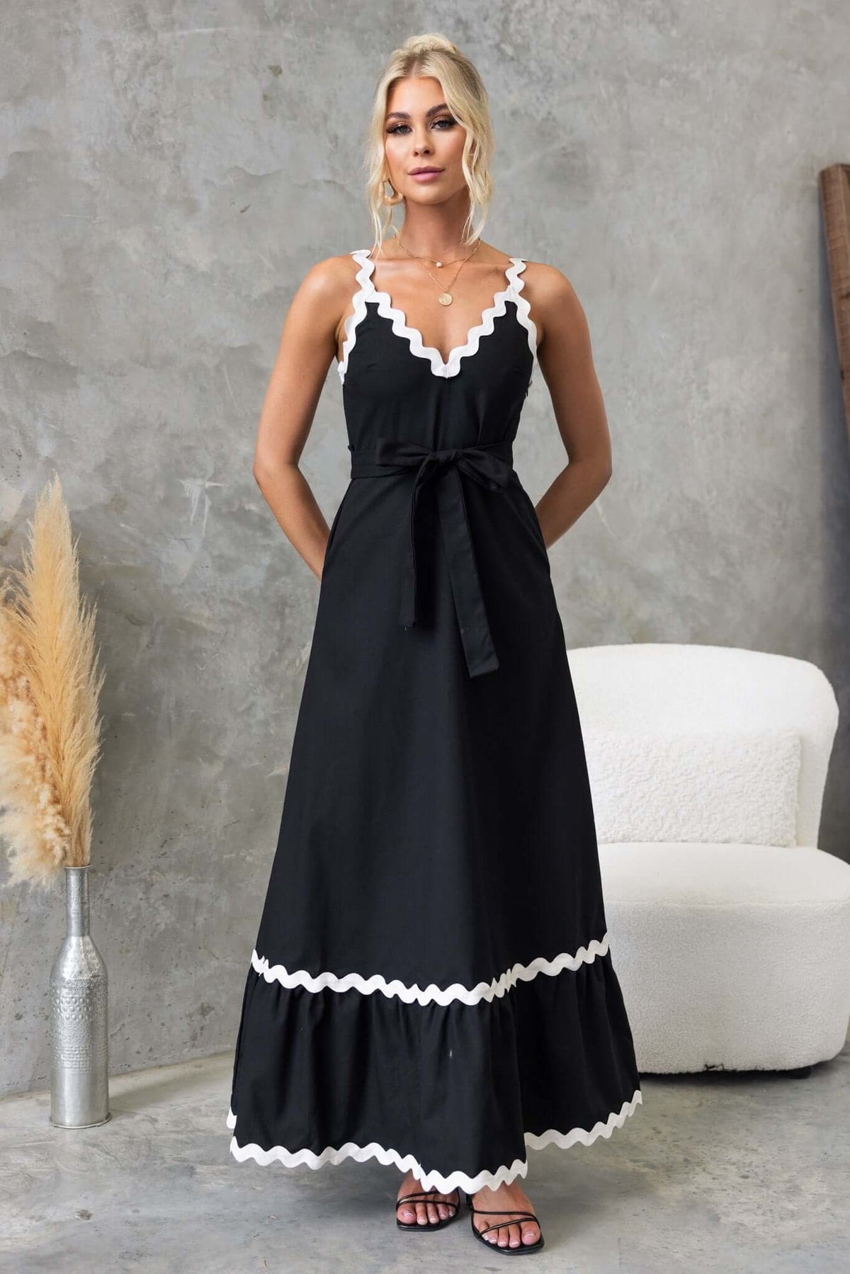 Stylish black maxi dress with a V-neckline, tie waist, and white scalloped trim, perfect for summer occasions.