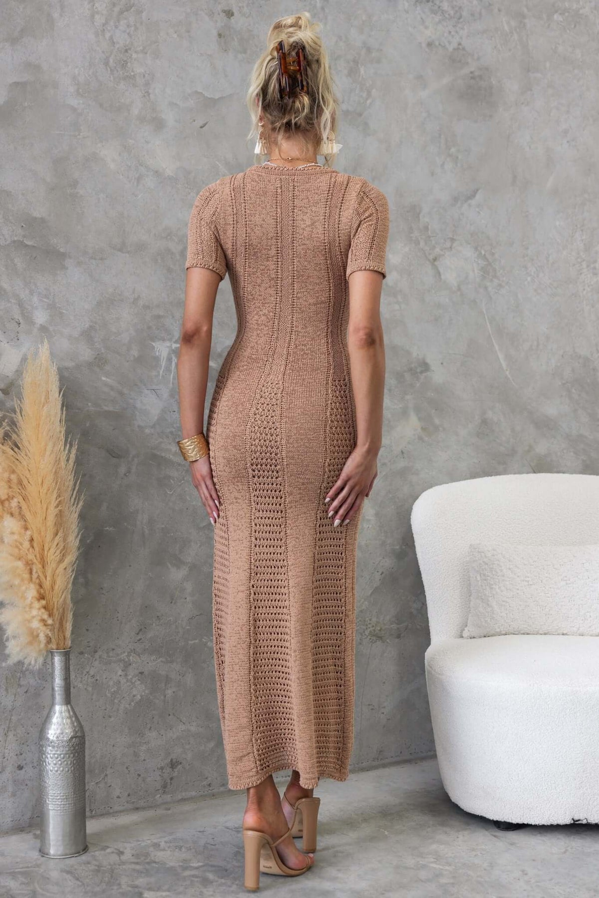 Model wearing a back view of a Qenna maxi dress in a soft tan color, showcasing its knit material and form-fitting design.