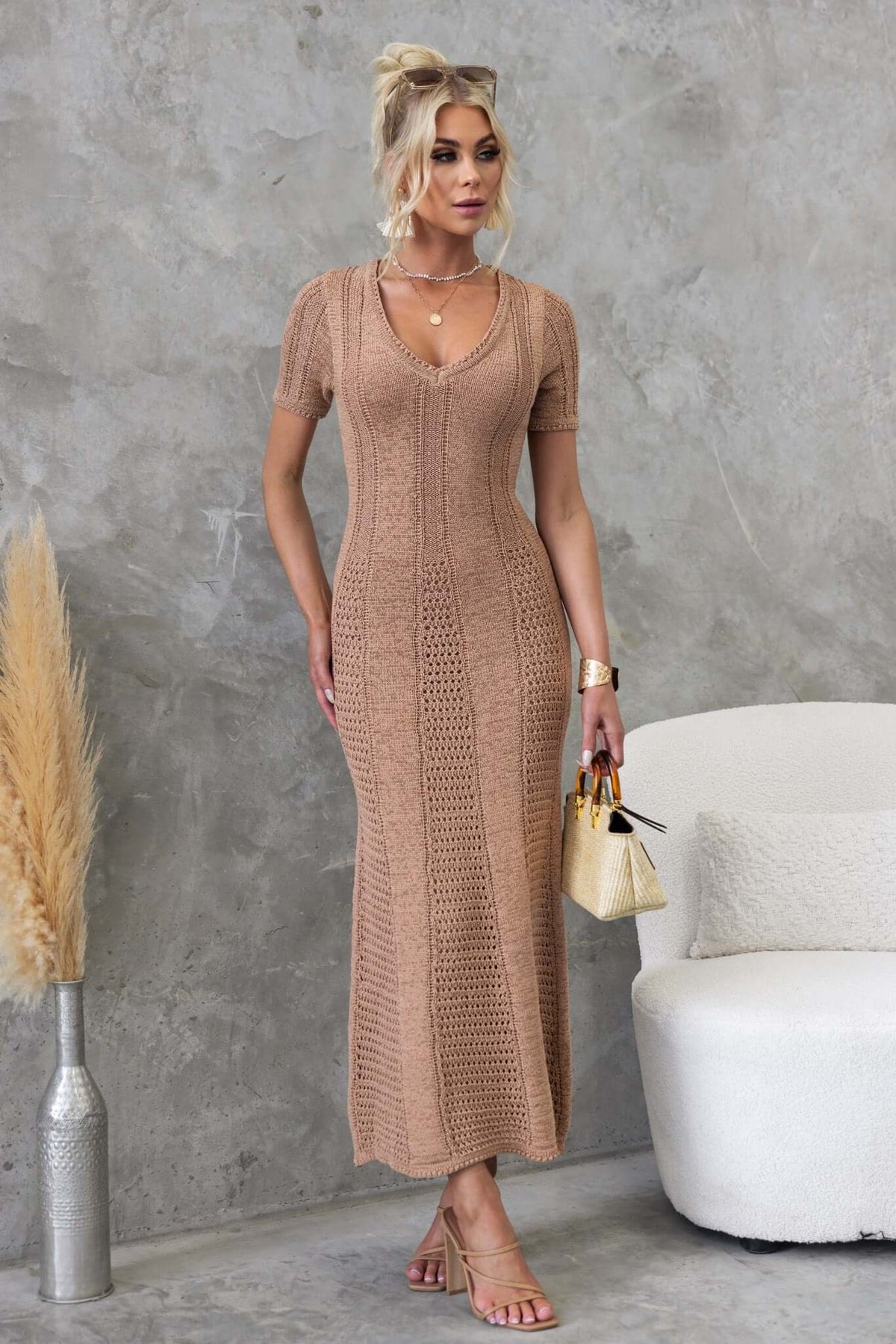 Woman in Qenna Maxi Dress with V-neckline, showcasing a knit design, posed in a modern interior setting.