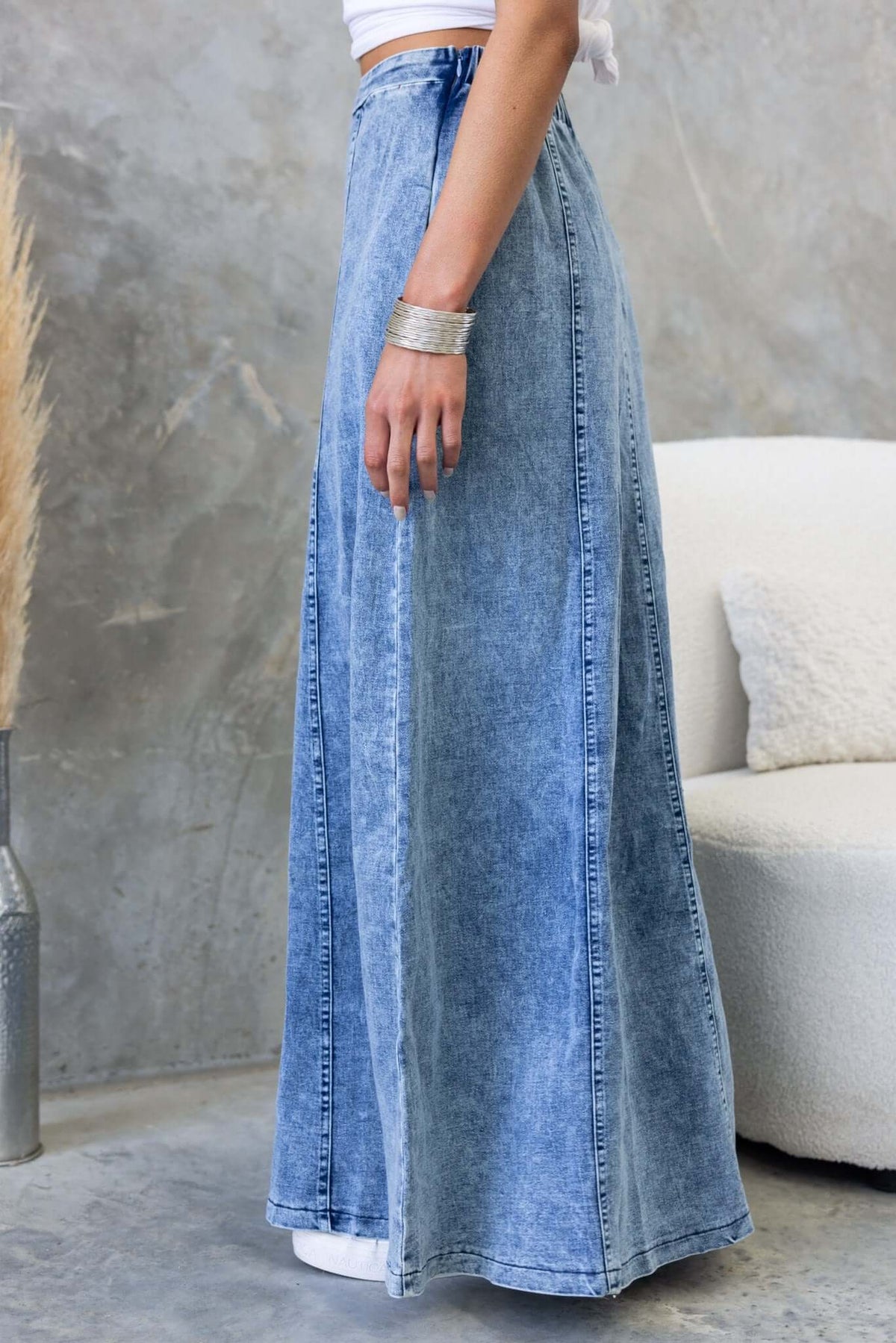 Side view of a woman wearing a Jacquie denim maxi skirt with a mid-high waist and a flowing design.