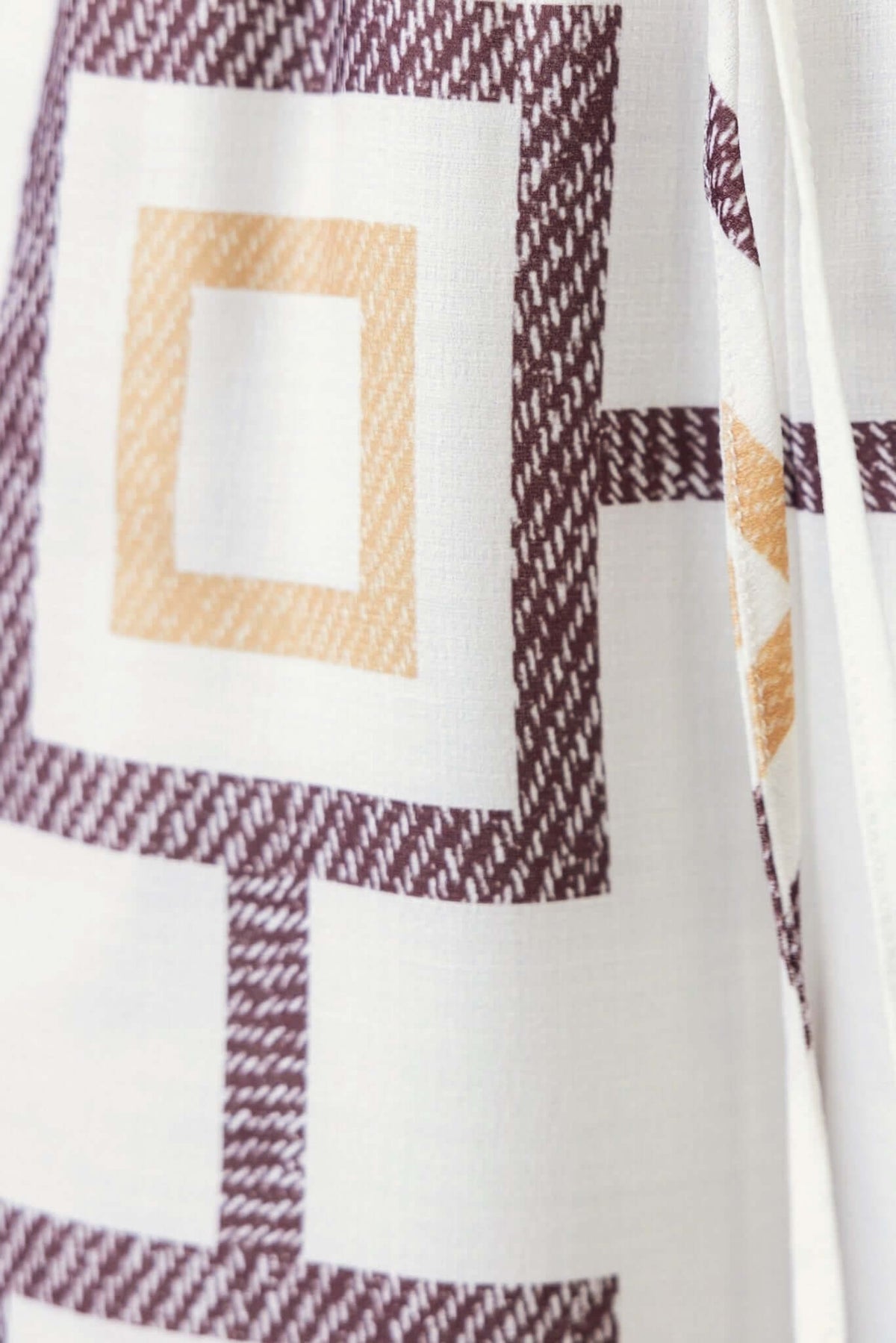 Close-up of fabric featuring a geometric pattern in cream, burgundy, and orange tones, perfect for stylish summer pants.