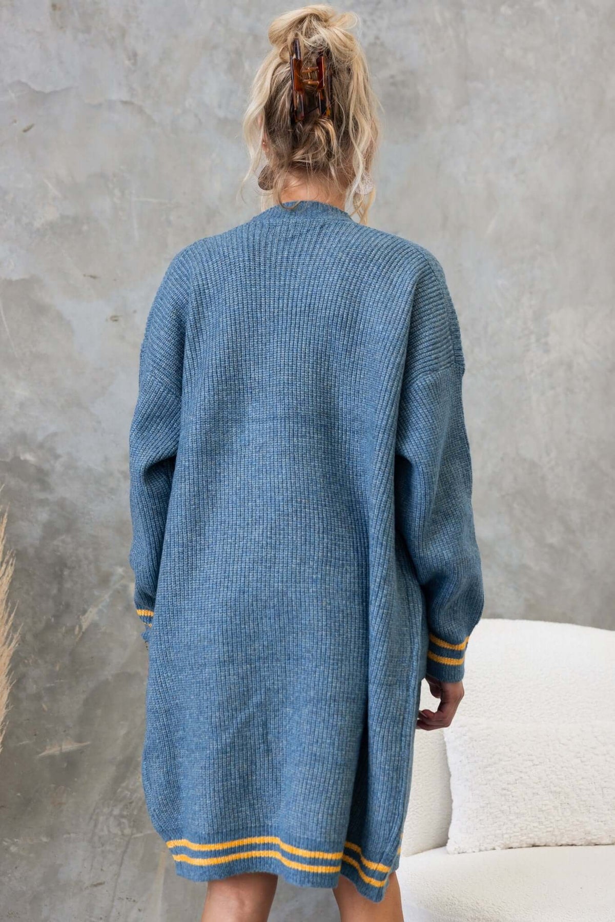 Back view of a longline blue cardigan with yellow and white stripes at the cuffs, showcasing a relaxed fit and knit design.