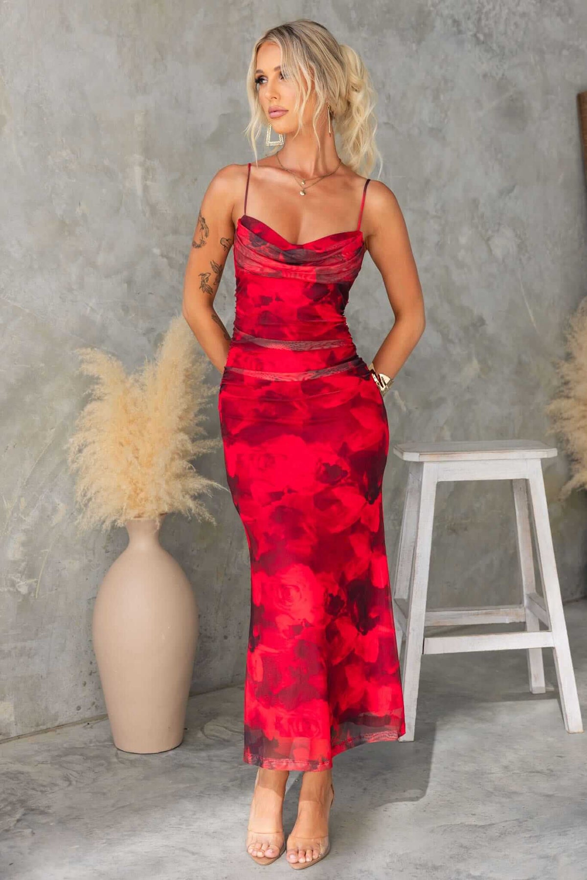 Model wearing an Emiliano Midi Dress in red floral print with adjustable straps, paired with nude heels.