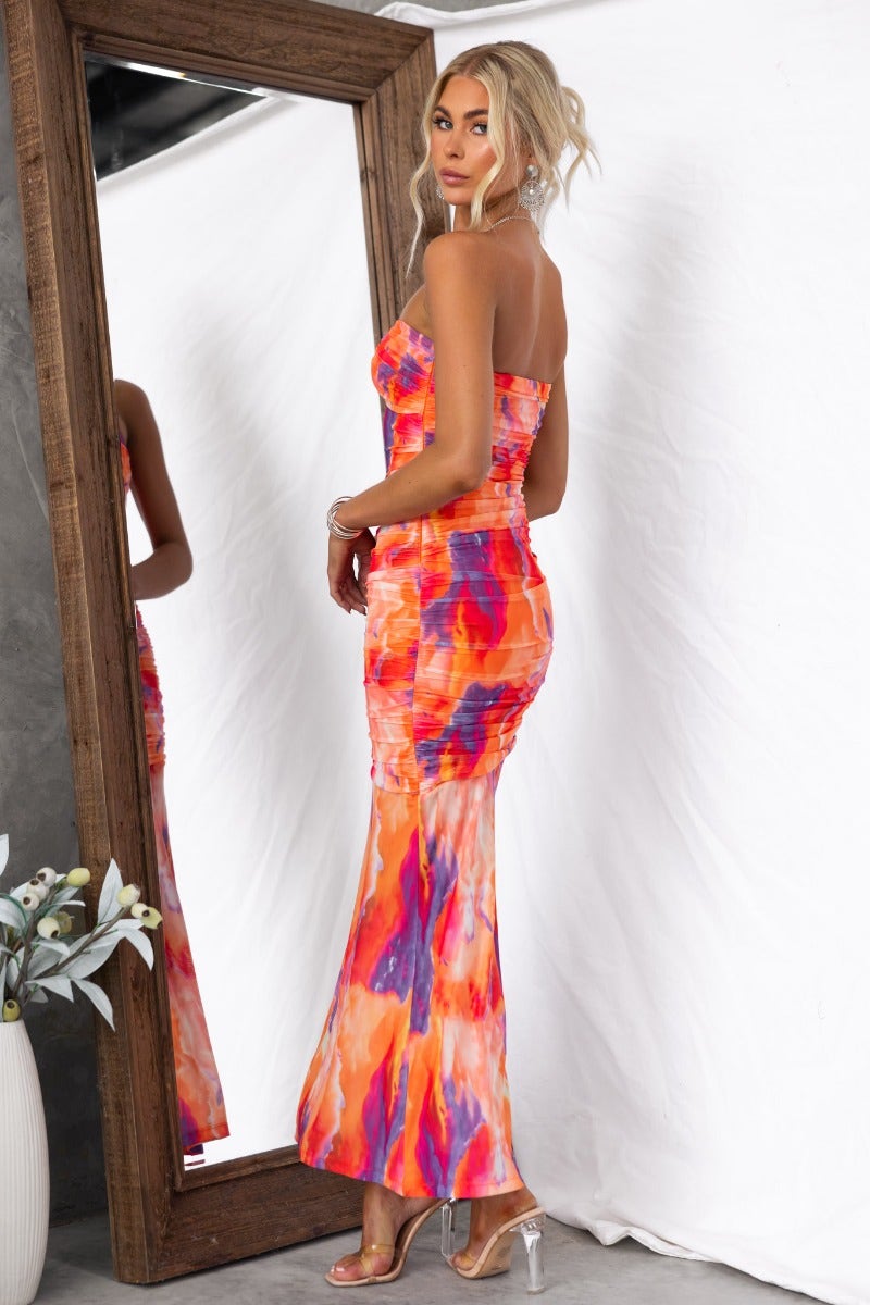 Strapless Obvious Maxi Dress in colorful tie-dye with ruching, side zip, and mesh overlay, worn by model in front of a mirror.