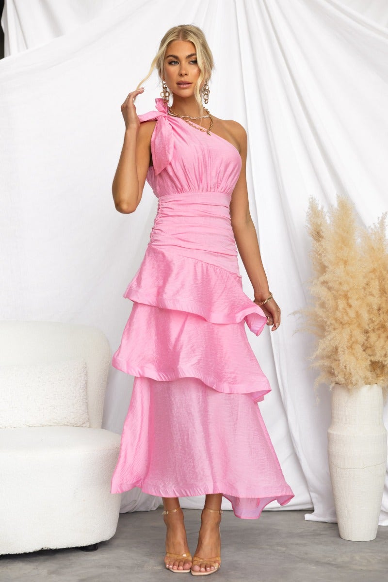 One-shoulder pink Sherbert Midi Dress with ruffle hem and tie detail, perfect for summer events. Model showcases size 6/XS.