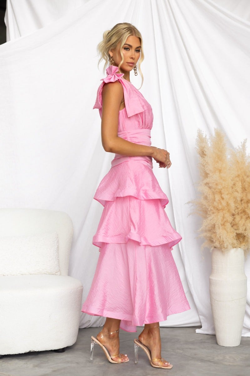 Model wearing a pink Sherbert midi dress with ruffle hem and one-shoulder neckline, styled against a neutral background.