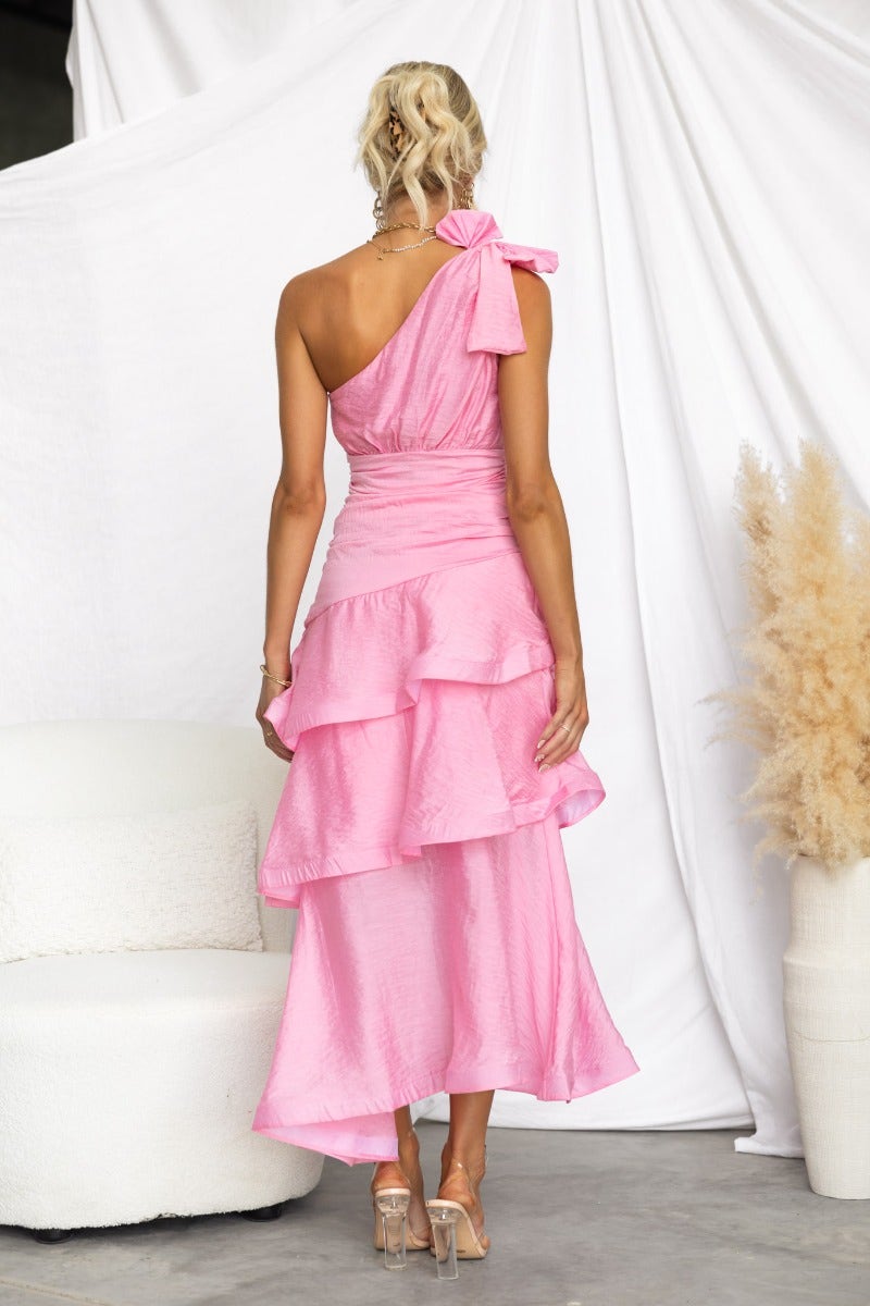 Back view of a pink Sherbert Midi Dress featuring a one-shoulder design and a ruffle hem, styled for a chic look.