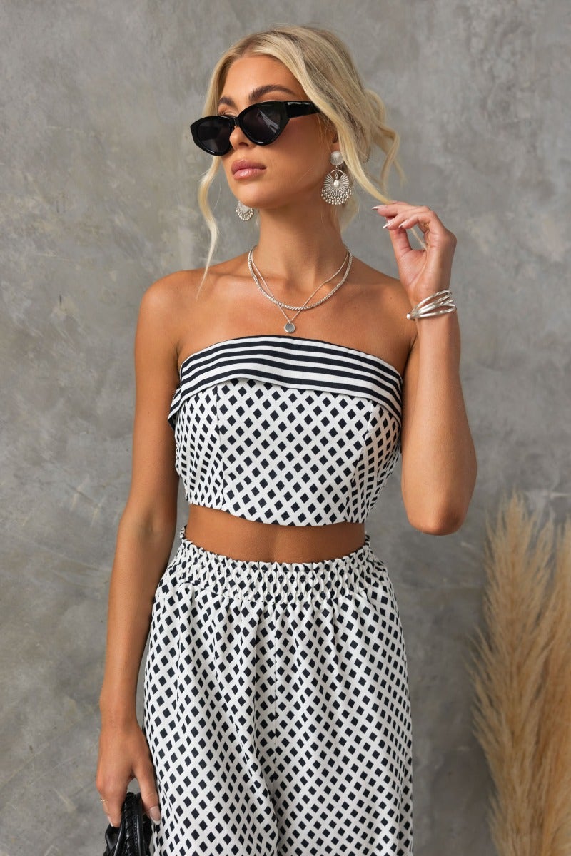 Stylish woman in a black and white strapless print top with sunglasses, showcasing a trendy summer look.