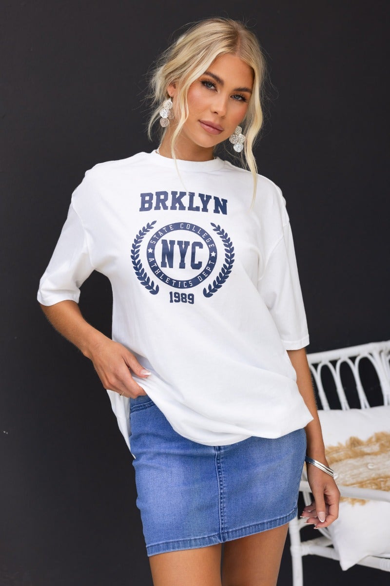 Model wearing Duke Top white tee with 'Brklyn NYC' print, paired with a denim skirt, showcasing an oversized fit.