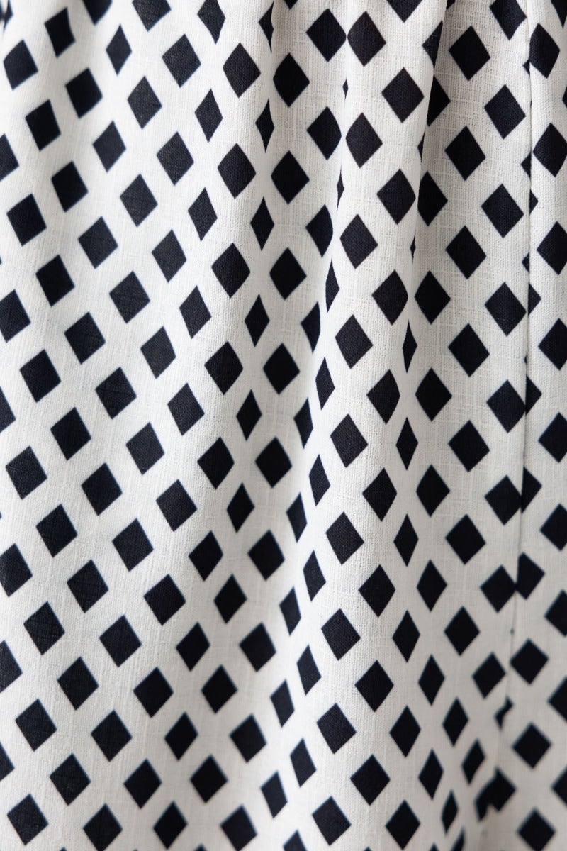 Close-up of fabric featuring a geometric black and white diamond pattern, ideal for stylish clothing applications.