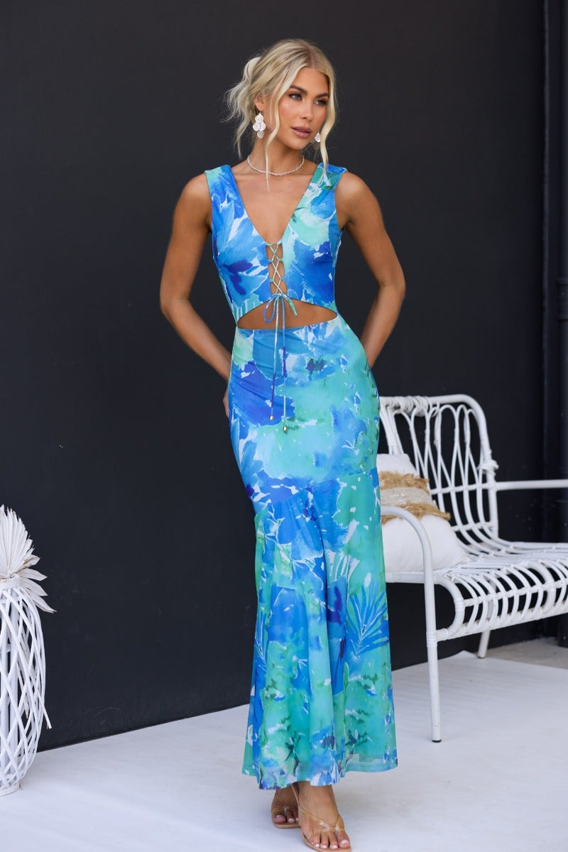 Model wearing a Pisces Maxi Dress with a V-neckline and tie detail, featuring a vibrant blue and green floral pattern.