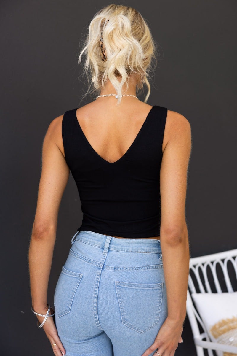 Back view of a woman in a black V-neck tank top paired with light blue high-waisted jeans against a dark background.