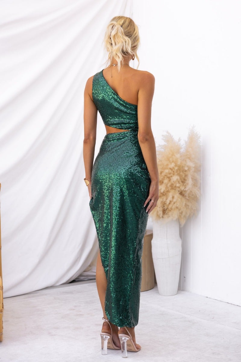 Back view of a woman in a green sequin one-shoulder maxi dress, styled with chic accessories and a sleek hairstyle.