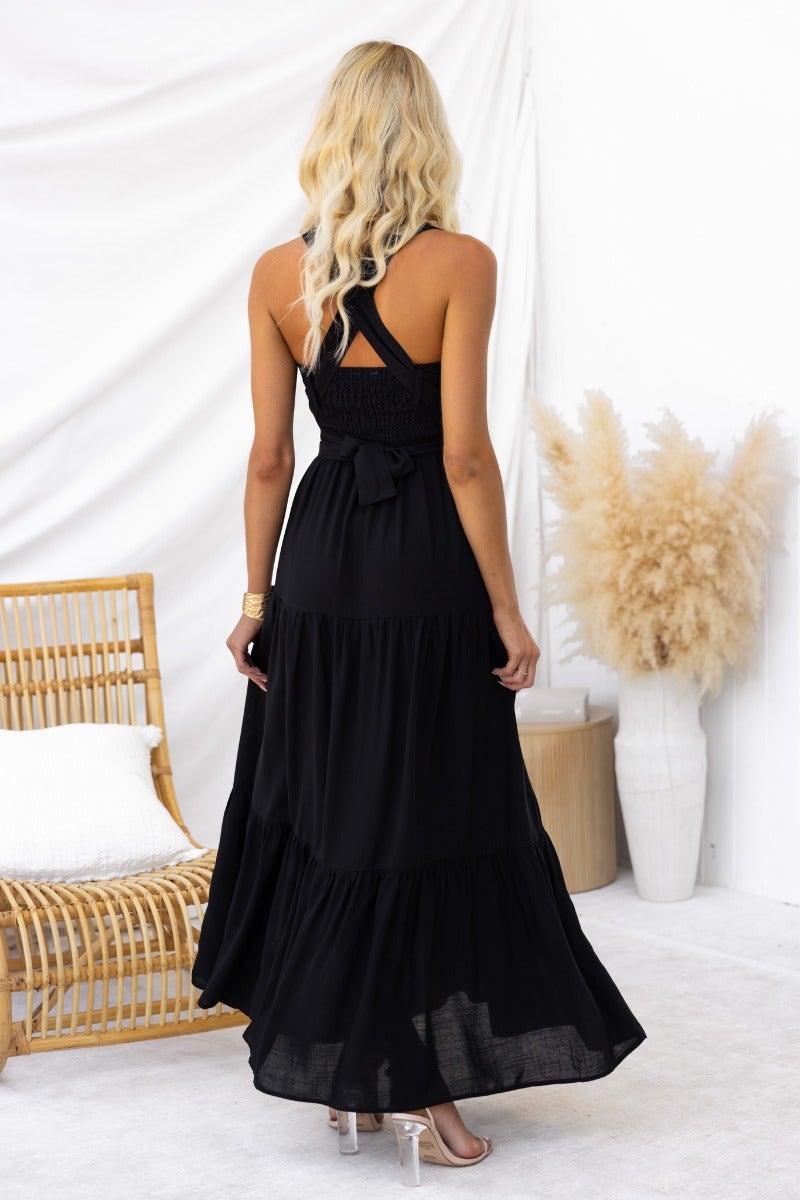 Back view of a woman wearing a black Etsie maxi dress with adjustable tie halter neckline and pockets.