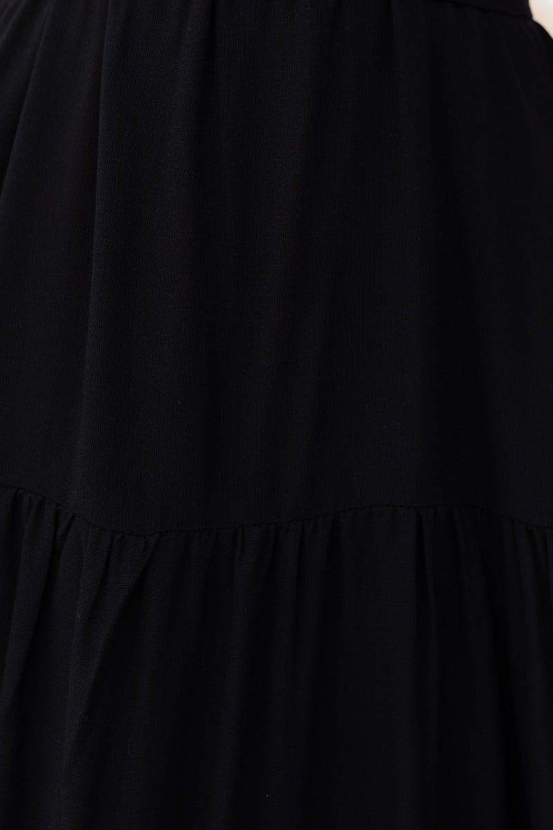 Close-up of the Etsie black maxi dress showcasing the fabric texture and tiered design in a flowing style.