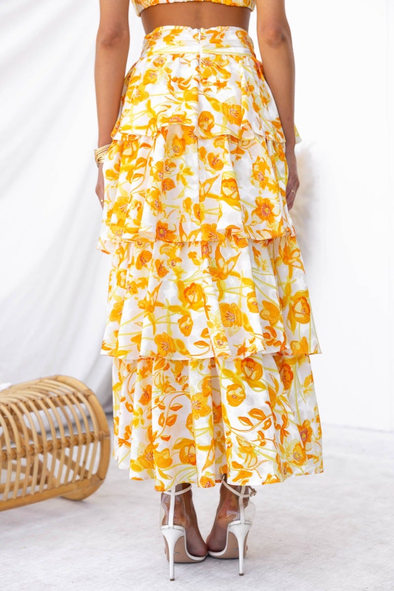 Back view of floral print Illusion Maxi Skirt with a ruffle design, showcasing layers of yellow and white fabric.