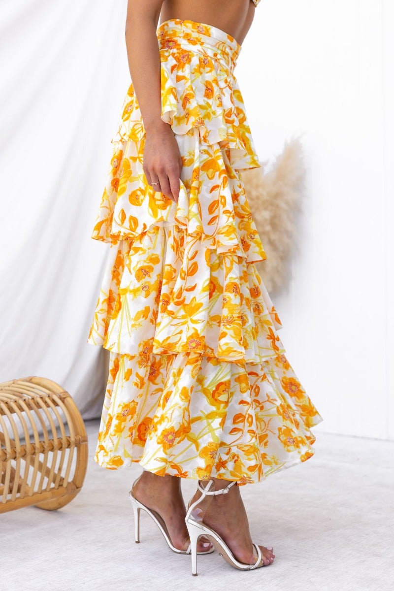 Floral print maxi skirt with ruffles and a mid-high waist fit, styled with strappy heels.
