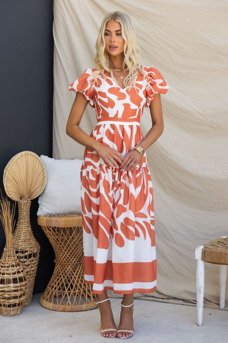 Naela Midi Dress with abstract print, V-neckline and puff sleeves, styled in a chic setting.