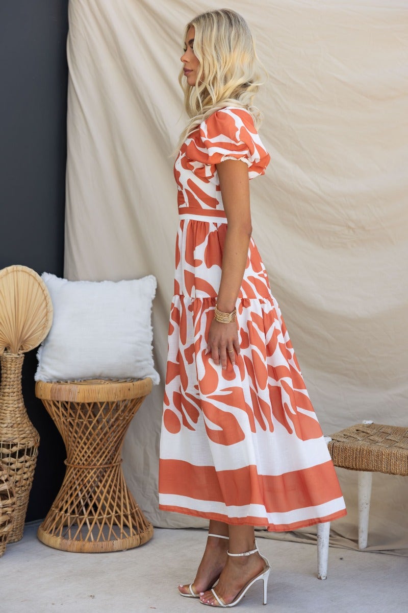 Model wearing the Naela Midi Dress featuring an abstract print, V-neckline, and puff sleeves against a neutral backdrop.