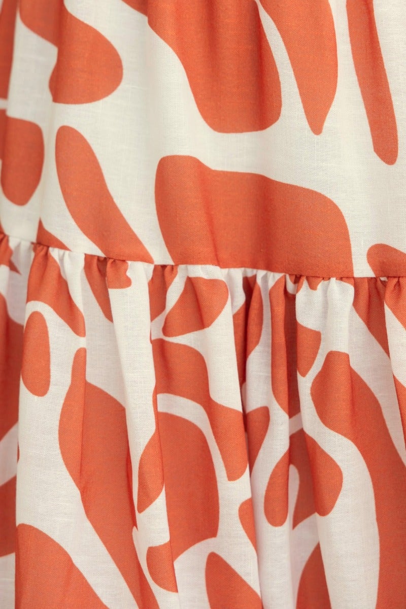 Close-up of Naela Midi Dress showing abstract orange and white print with ruffled hem detail.