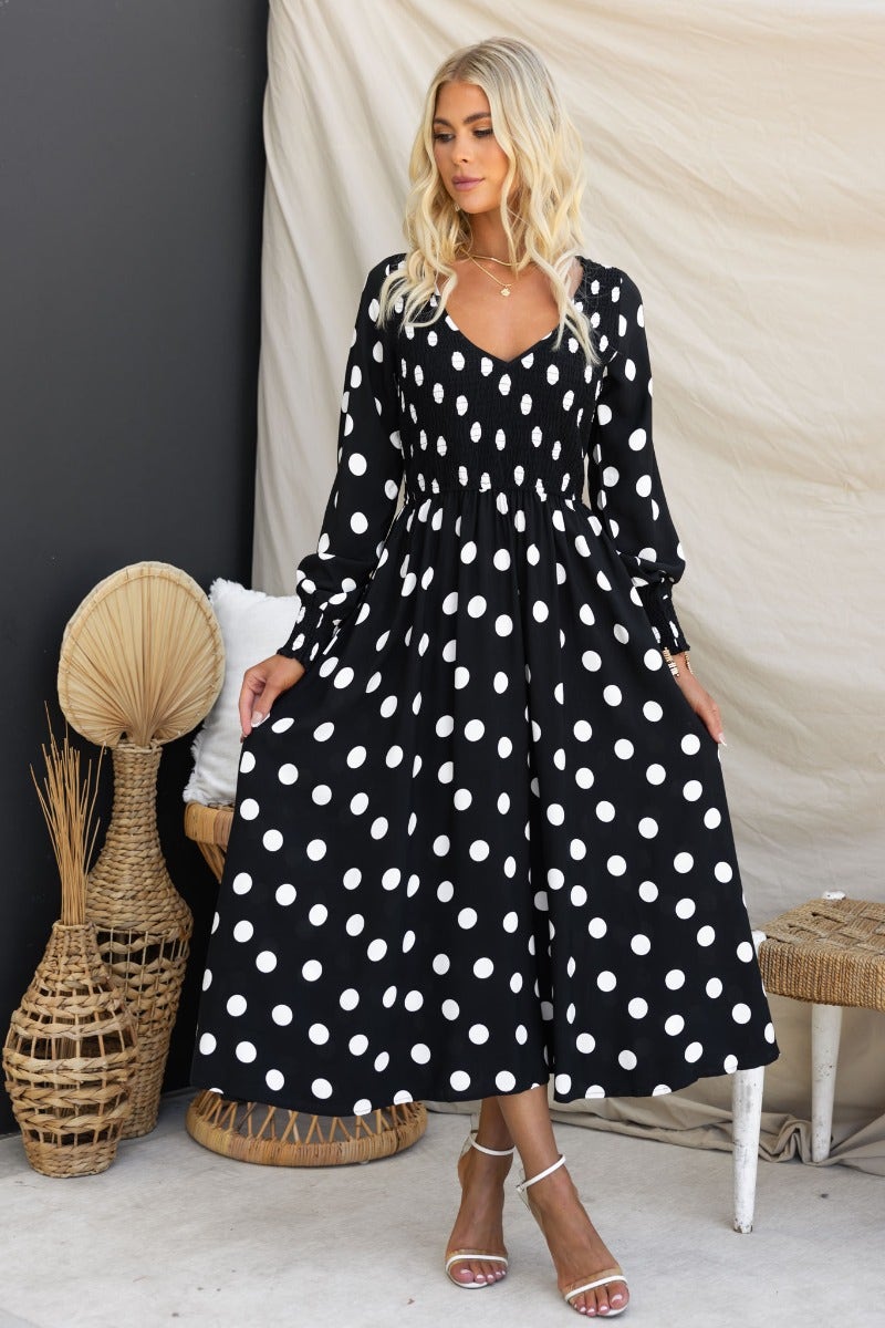 Black polka dot midi dress with V-neckline and elasticized bodice, styled on a model.